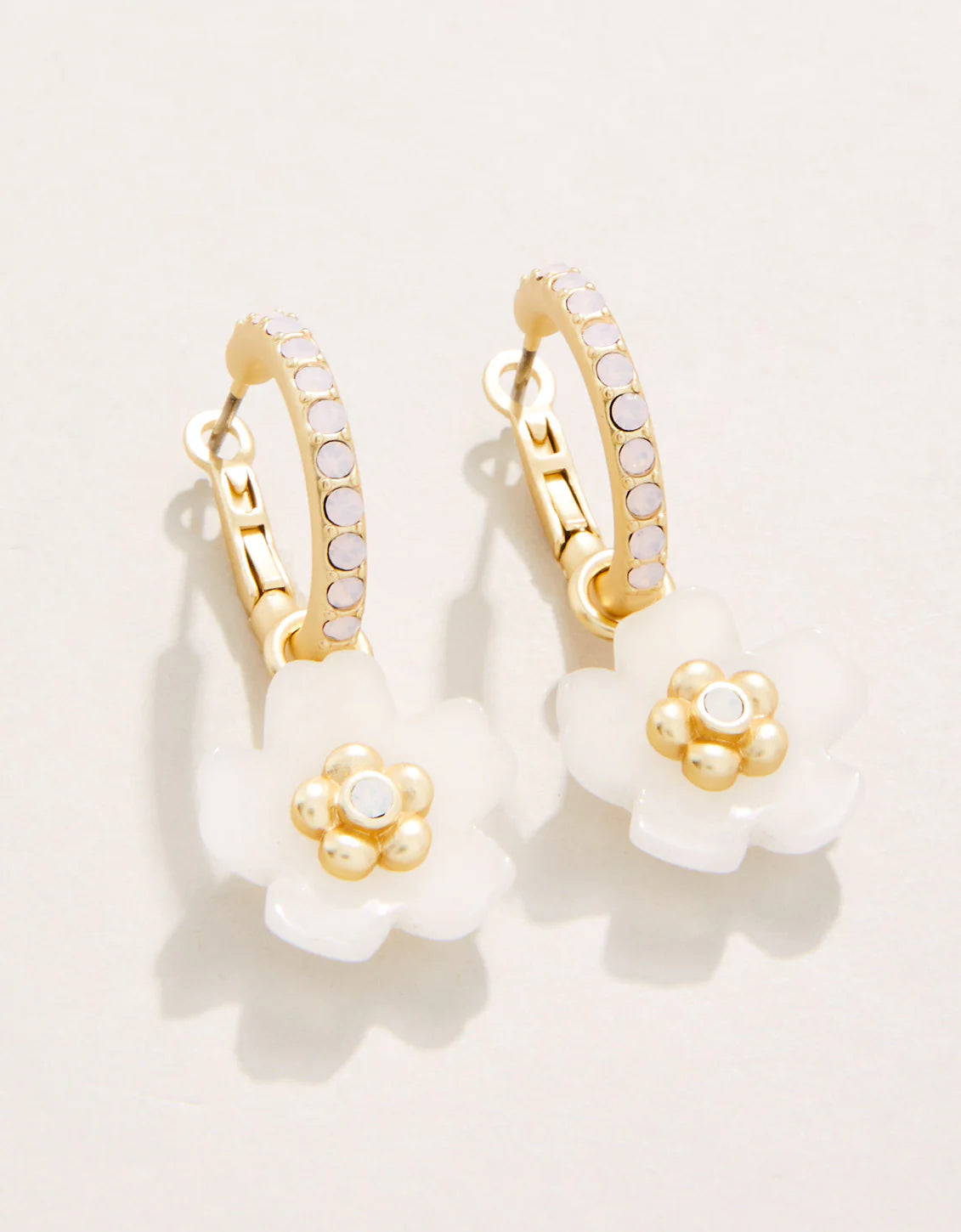 A pair of white and gold floral design earrings with a lever back post hoop closure.