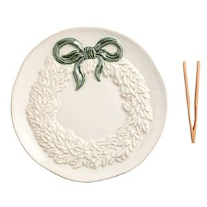 Decorative plate with a wreath design and a green bow, accompanied by wooden chopsticks on a white background.