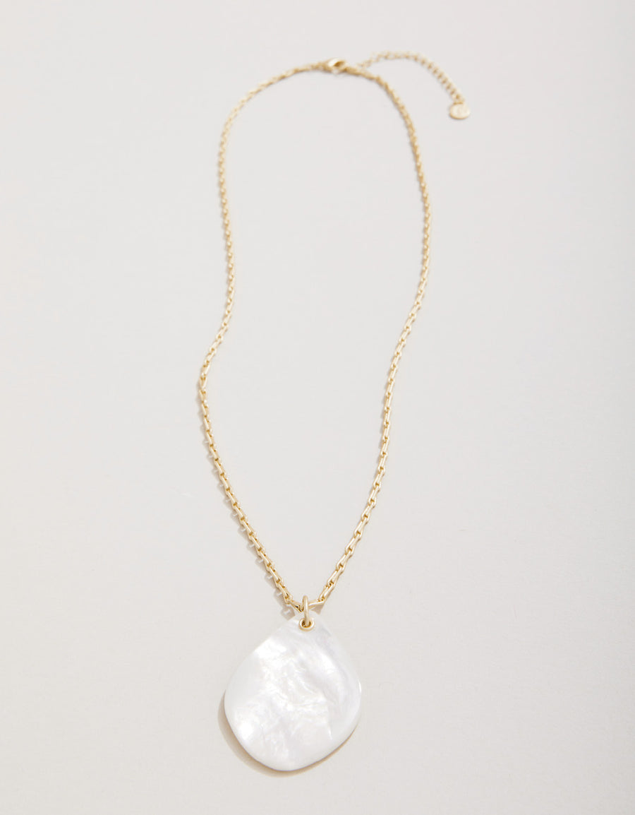 Gold necklace with a large white pendant on a light gray background