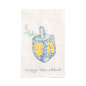 An off-white fabric tea towel featuring a watercolor illustration of a Hanukkah dreidel with a blue and white pattern, yellow Hebrew letters, green leaves, and the text 'Happy Hanukkah' in blue script.