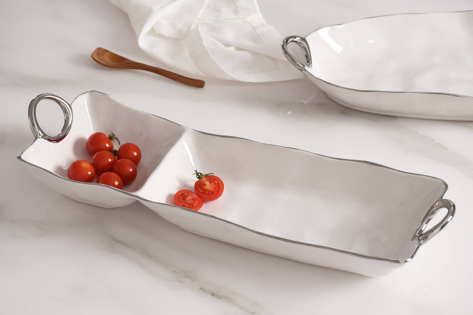 White ceramic dish with handles containing cherry tomatoes on a marble surface.