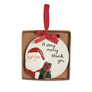 A round white ceramic Christmas ornament featuring a 3D Santa Claus figure and the text 'A very merry thank you', presented inside a brown gift box with a red ribbon loop.