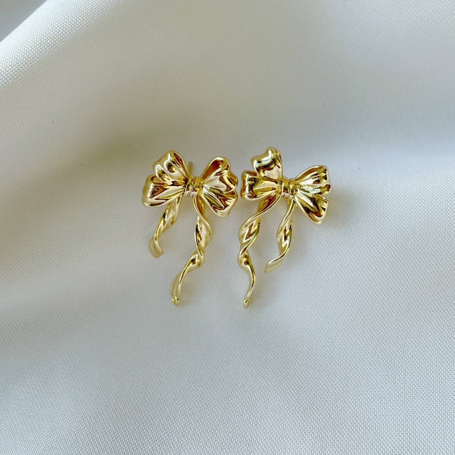 Gold bow-shaped earrings on a light fabric background