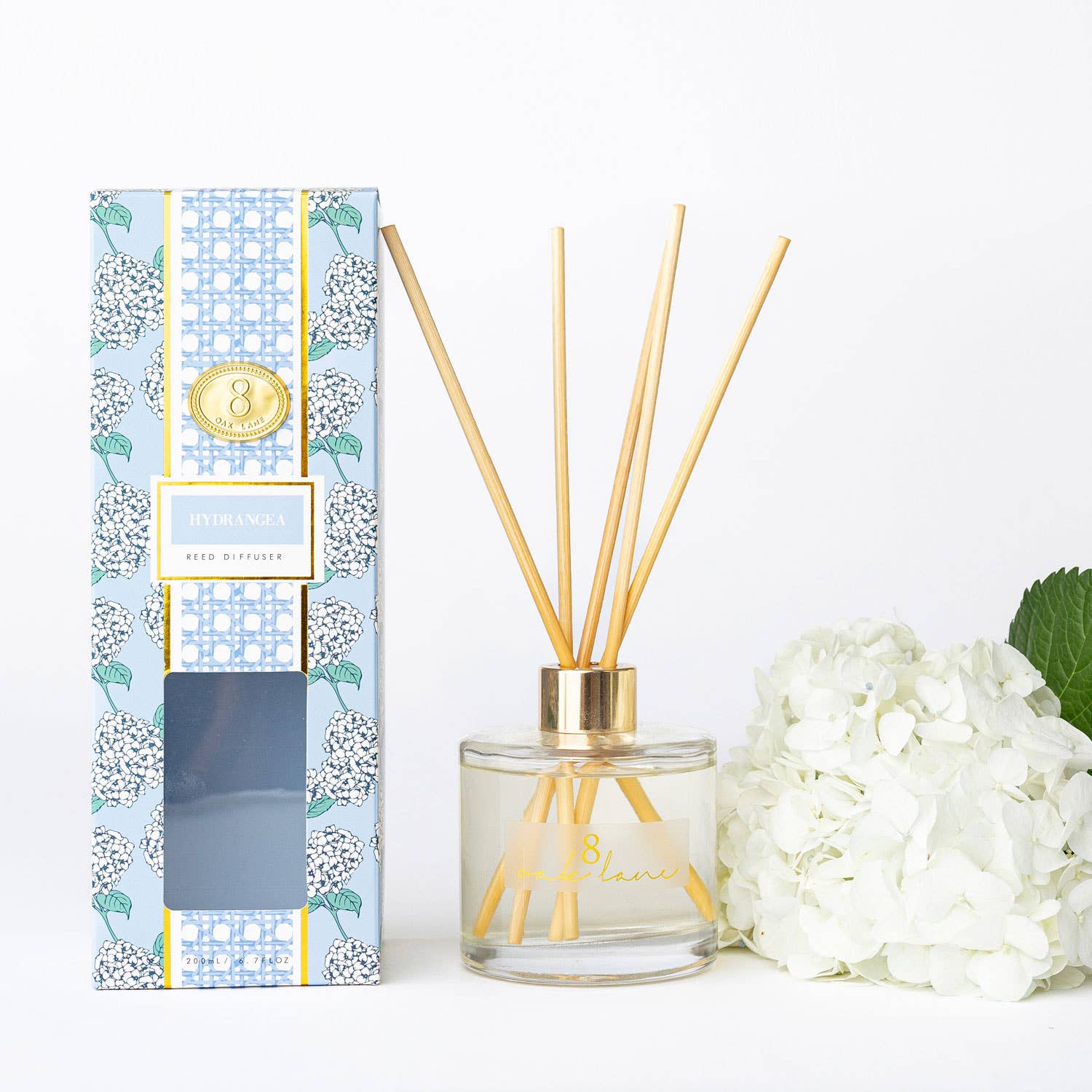 Reed diffuser with floral packaging and white flowers on a light background