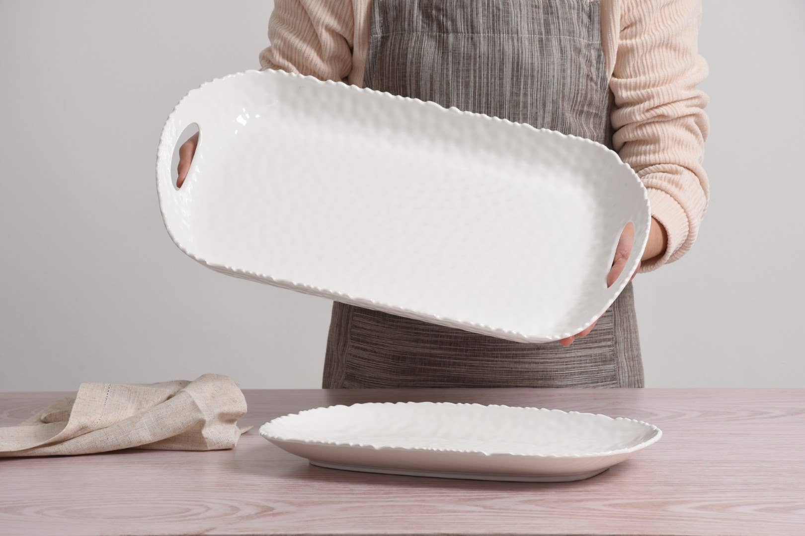 Person holding a white ceramic serving dish on a wooden table.