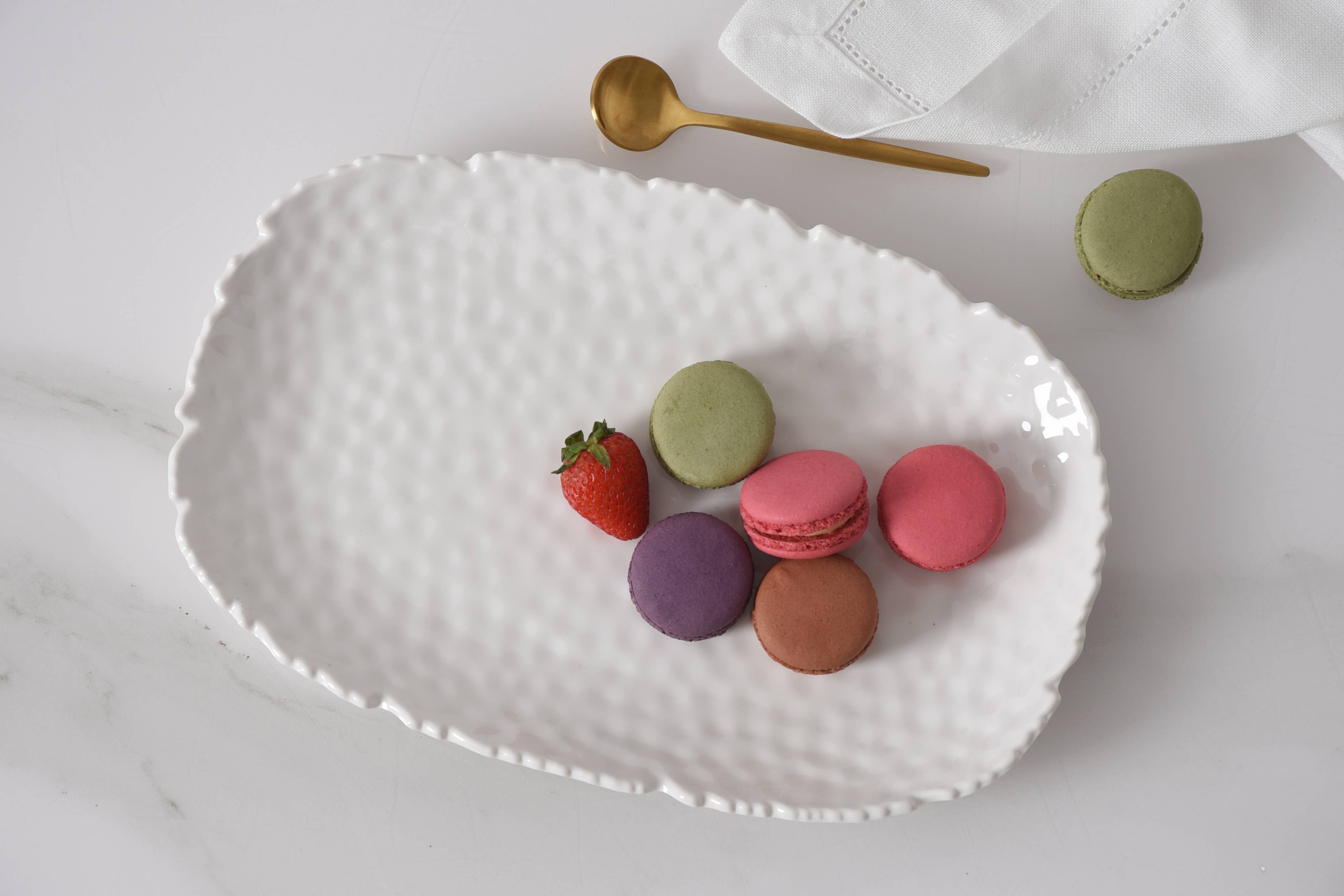 White textured platter with colorful macarons and a strawberry on a light background