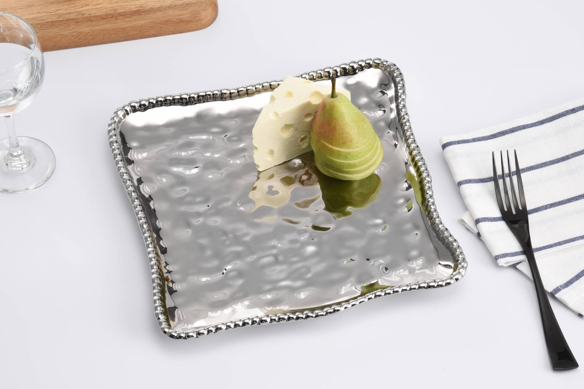 Metallic square tray with two pears on a white surface with a fork and napkin.