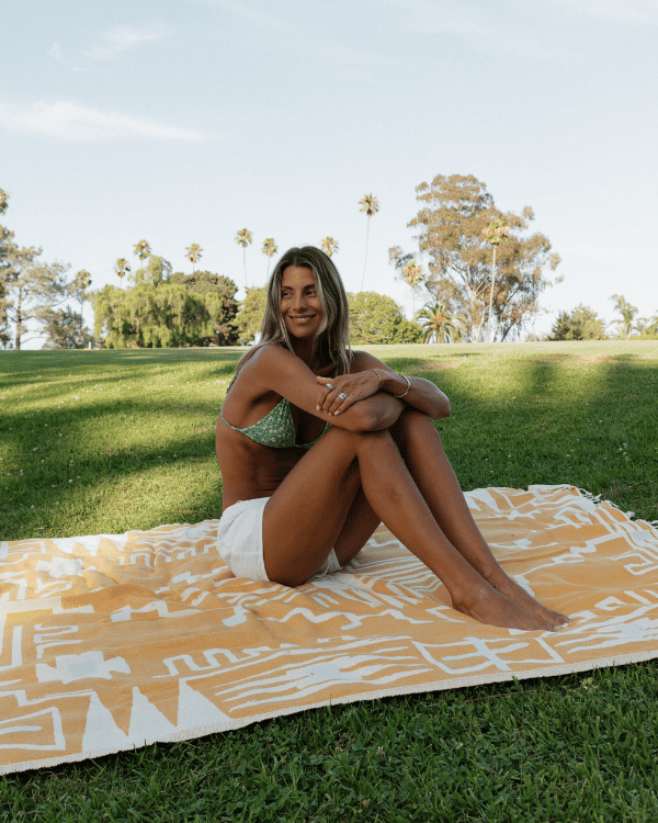 Woman in a bikini sitting on a yellow patterned blanket in a park