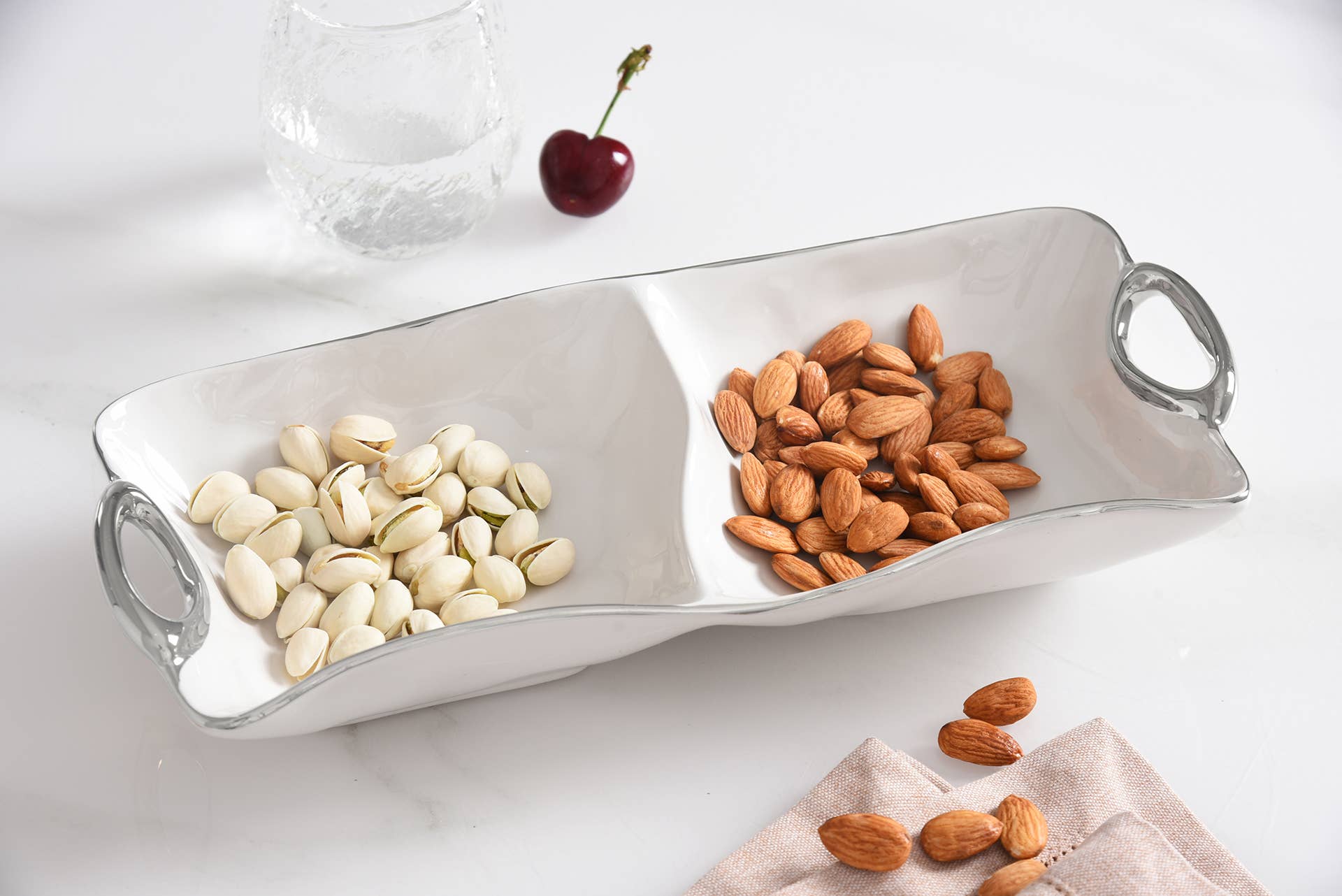 Divided silver tray with almonds and pistachios on a white surface
