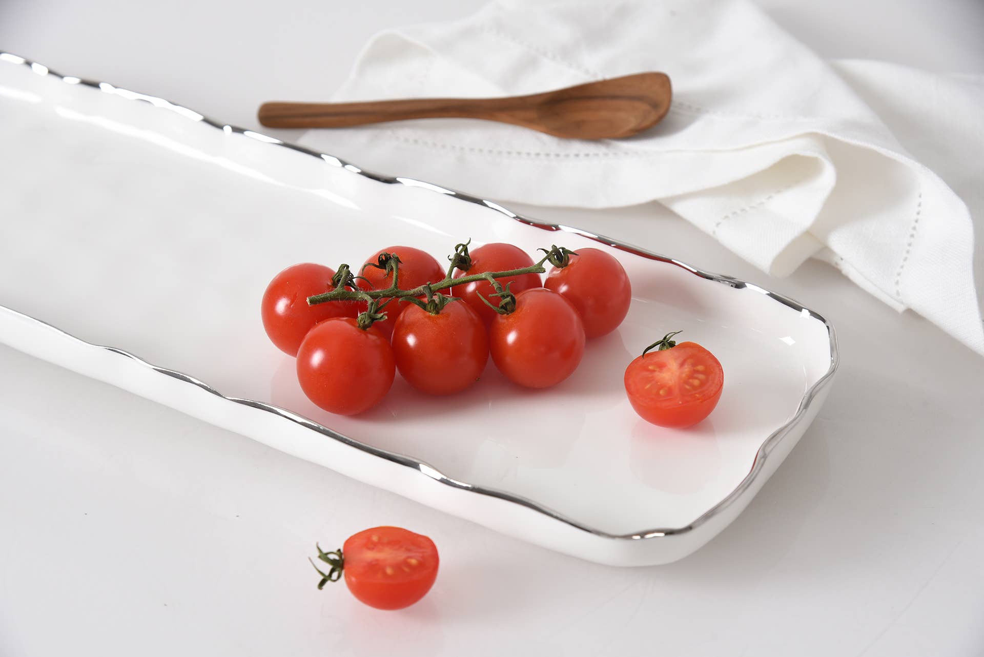 Tomatoes on a white plate with a wooden spoon on a white cloth background