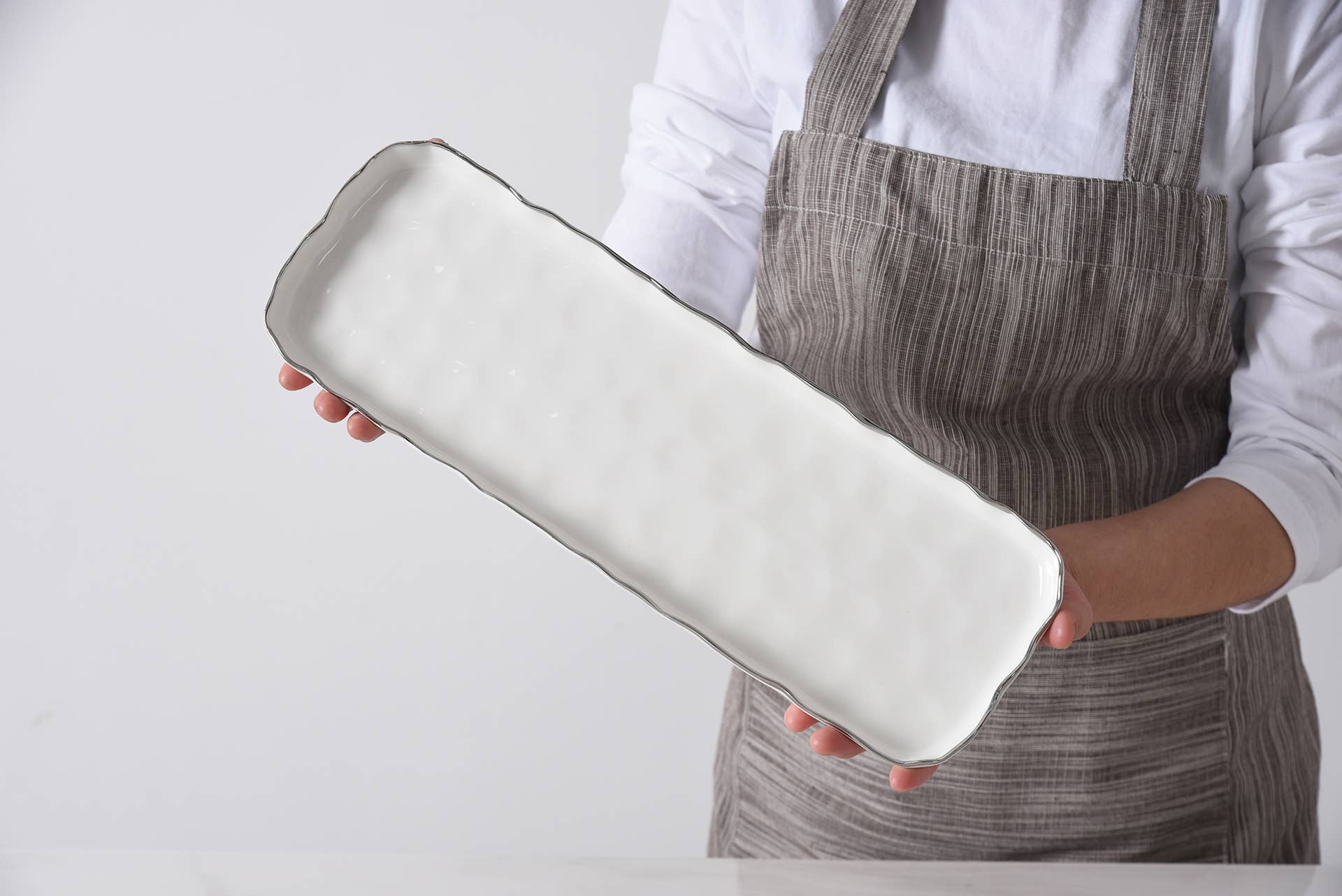 Person holding a long, thin ceramic dish against a plain background