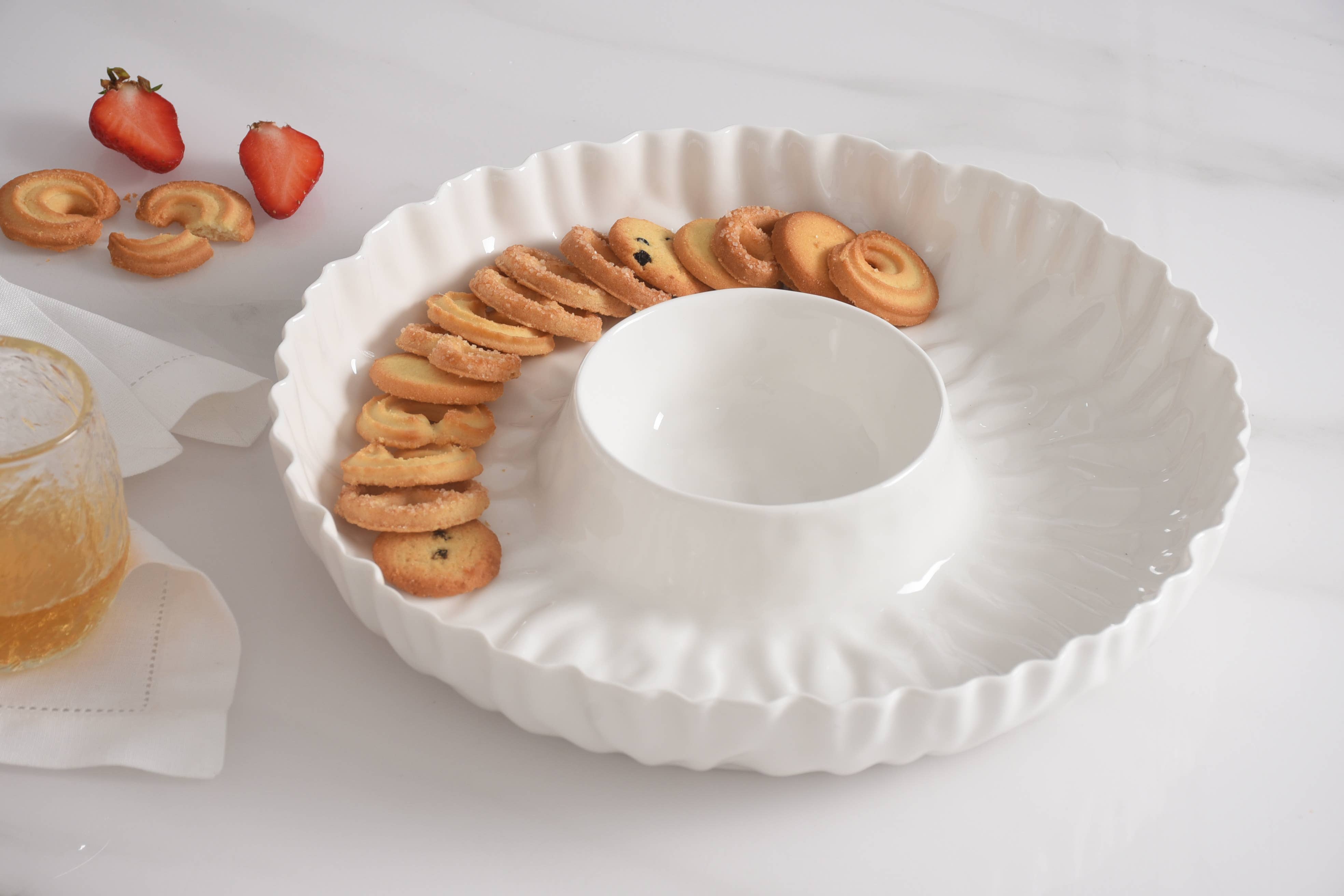 White ceramic dish with cookies arranged around a central round dish on a white surface.