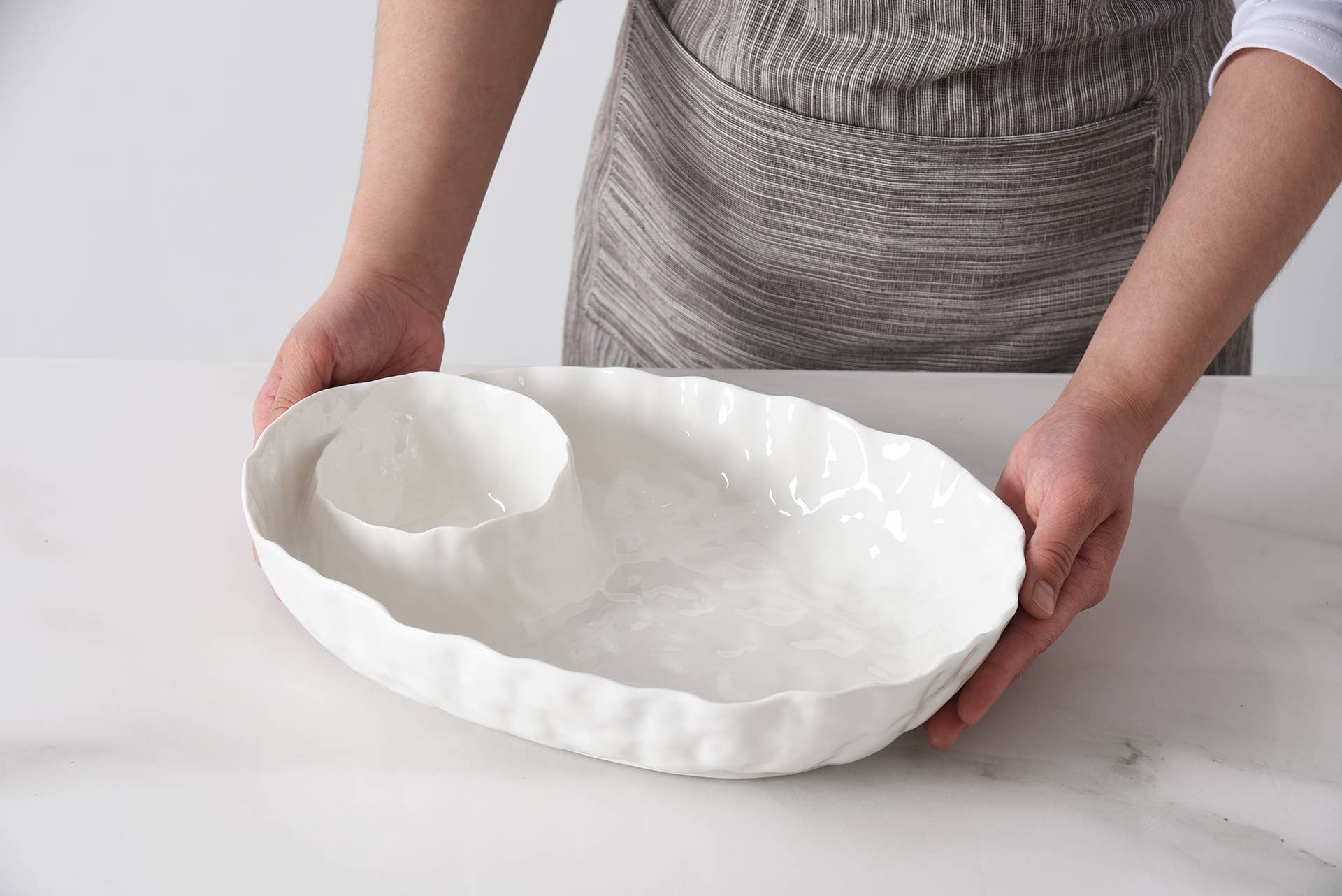 Person holding a white ceramic dish on a light background