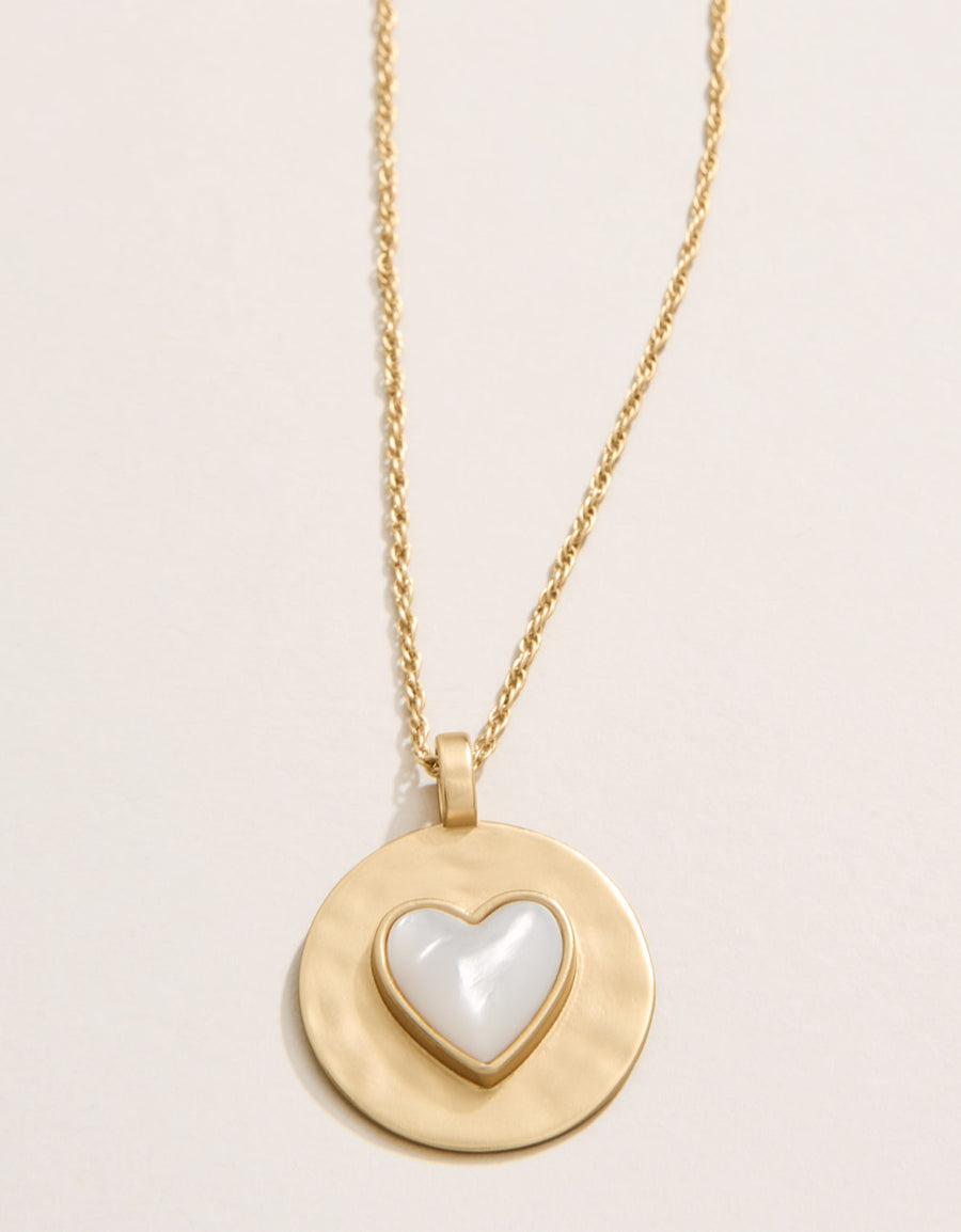 Gold necklace with a heart-shaped pendant on a light beige background
