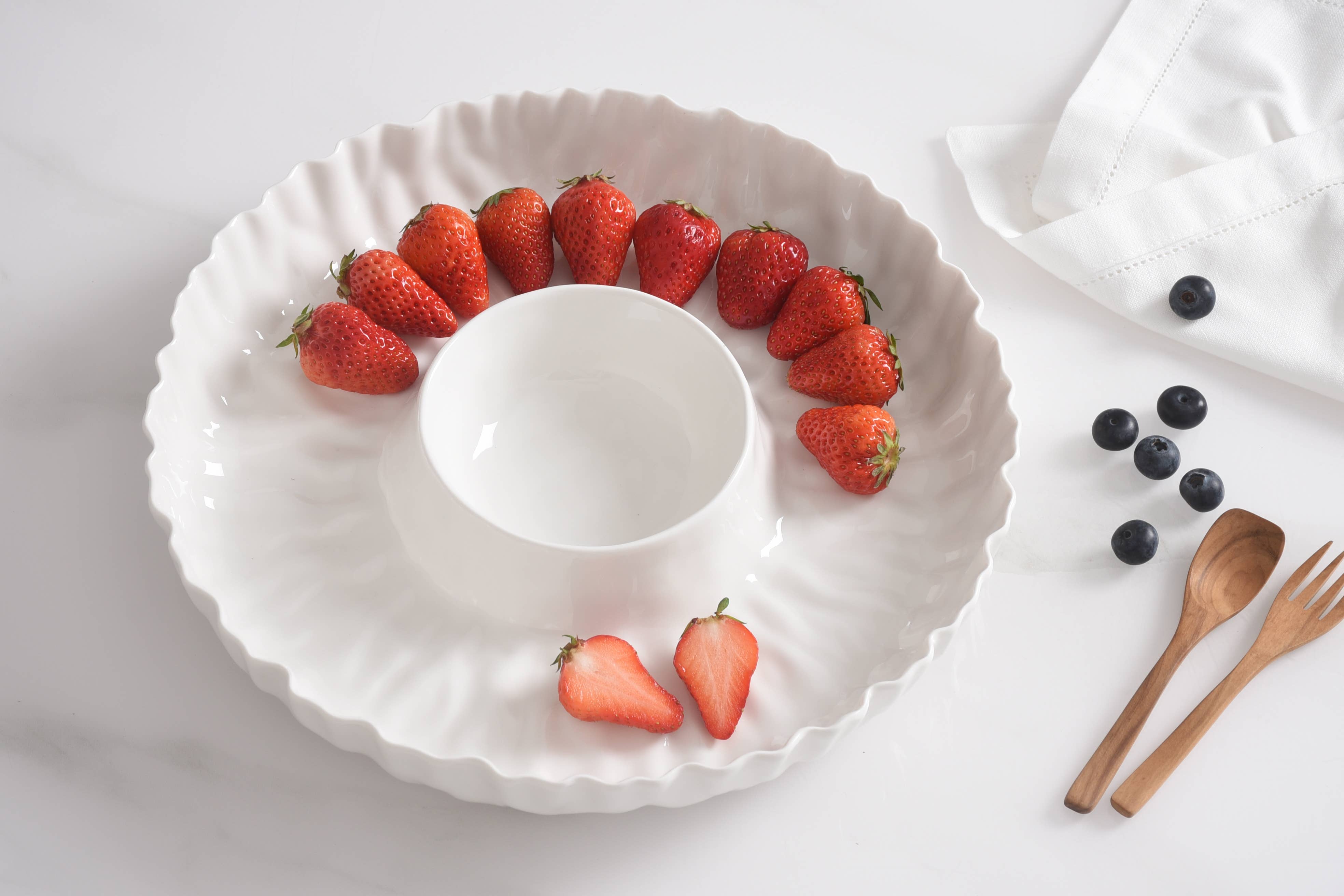 White decorative plate with strawberries arranged around a central bowl on a light surface.
