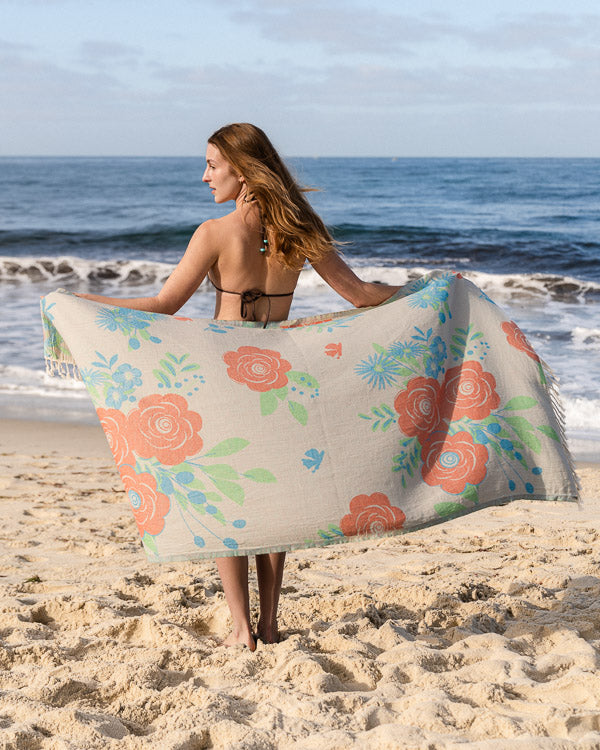 Woman on a beach holding a floral towel with ocean waves in the background