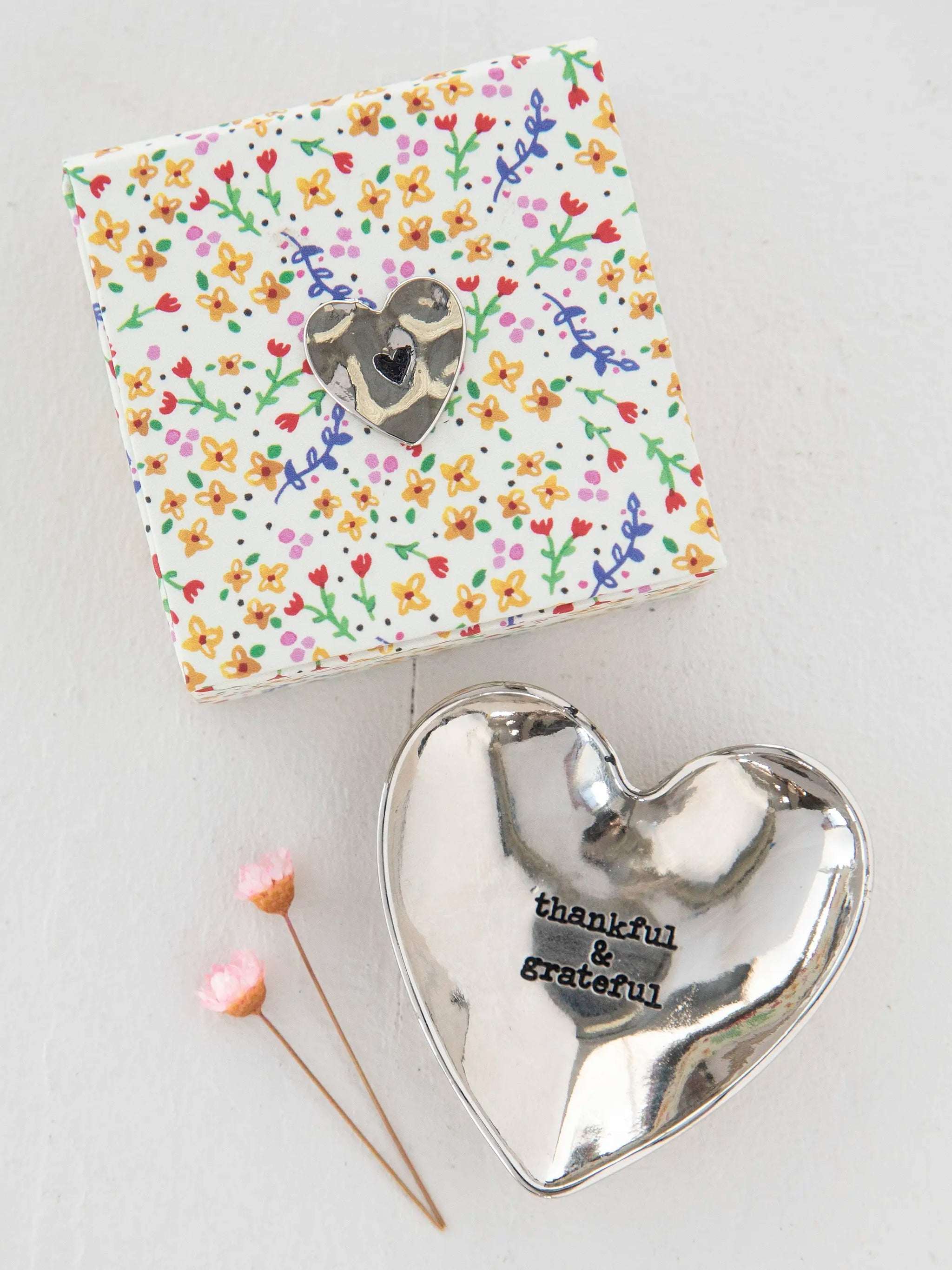Heart-shaped silver dish with 'thankful & grateful' text, next to a floral-patterned box on a white background