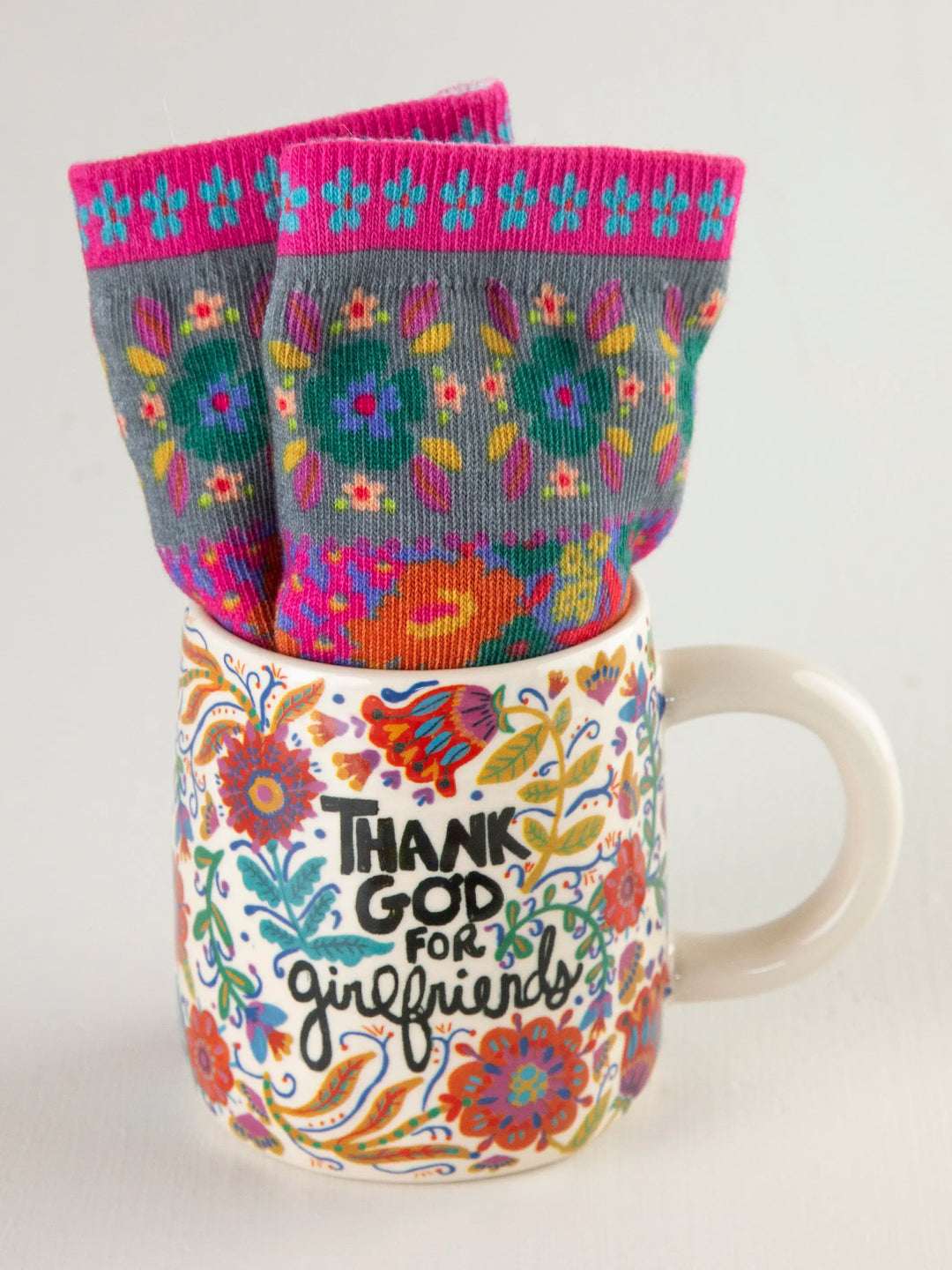 Colorful mug with floral design and text, paired with patterned socks on a white background