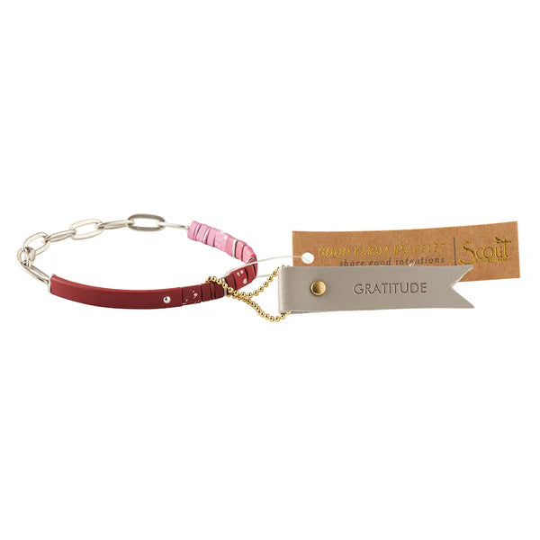 A red and silver bracelet with a chain, featuring matte beads with ombre design and a leather keychain hangtag with 'Good Karma' engraved on it.