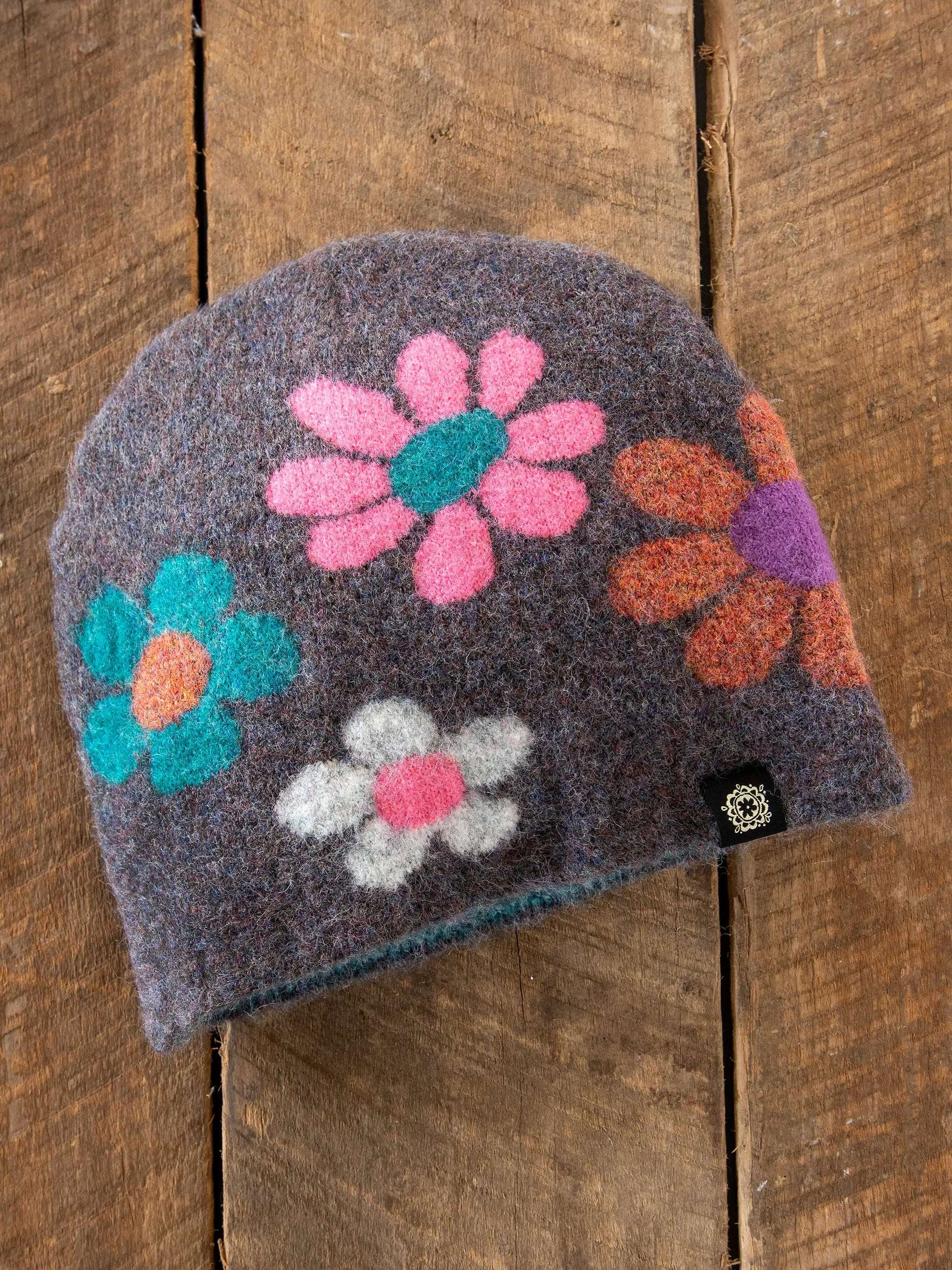 Gray knit beanie with colorful flower patterns on a wooden surface