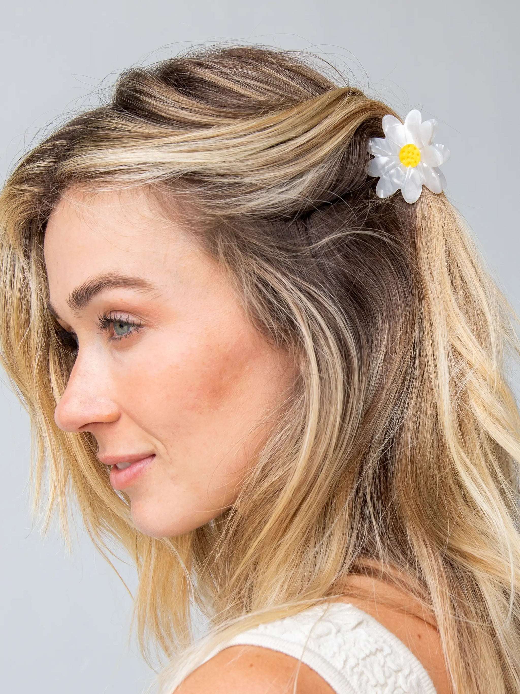 Woman with blonde hair featuring a white flower clip against a light gray background