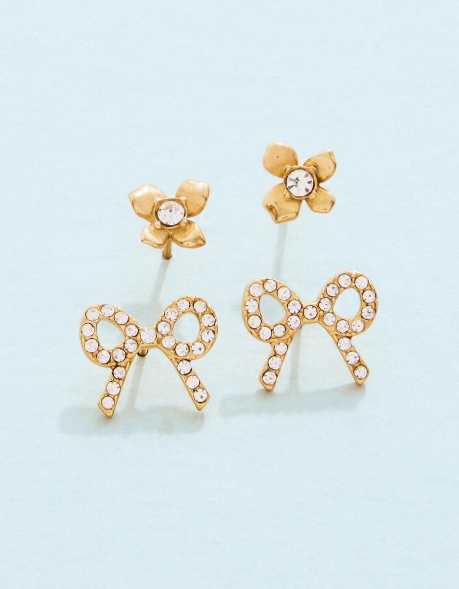 Gold bow-shaped earrings with clear stones on a light blue background