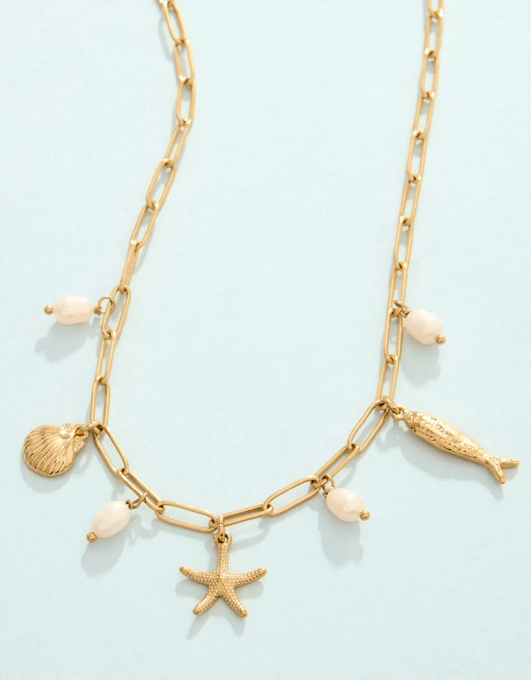 Gold chain necklace with shell and starfish charms on a light blue background