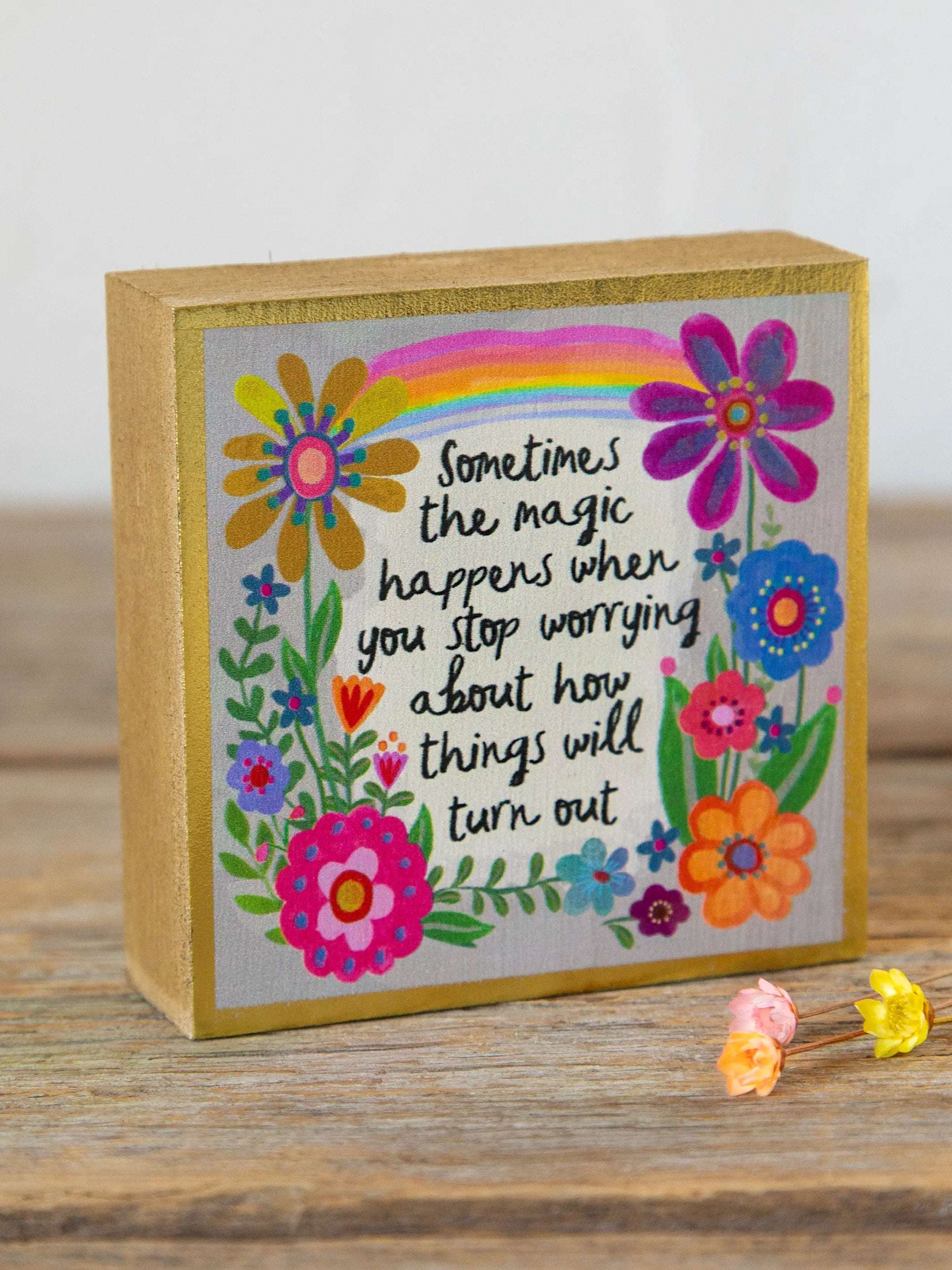Decorative box with colorful flowers and a rainbow, featuring a motivational quote on a wooden surface.