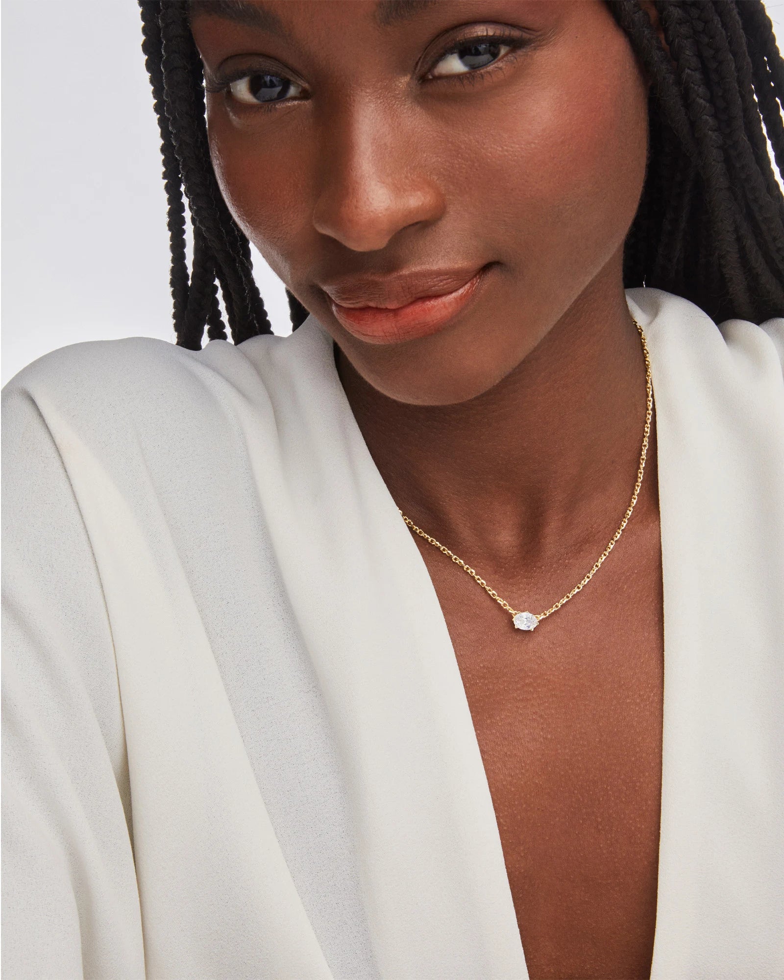 Woman wearing a gold necklace with a white pendant against a neutral background
