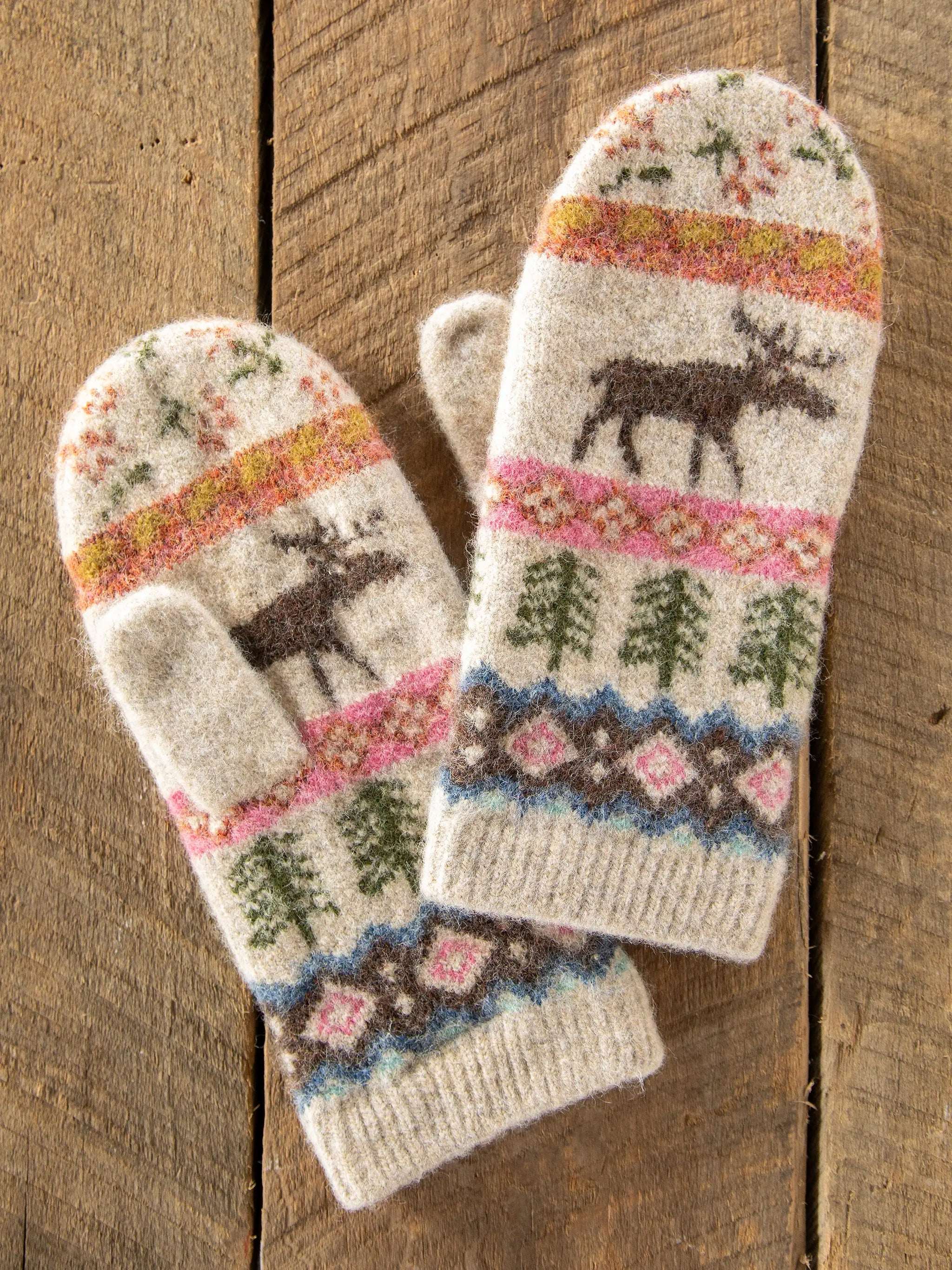 Pair of knitted mittens with moose and floral patterns on a wooden surface