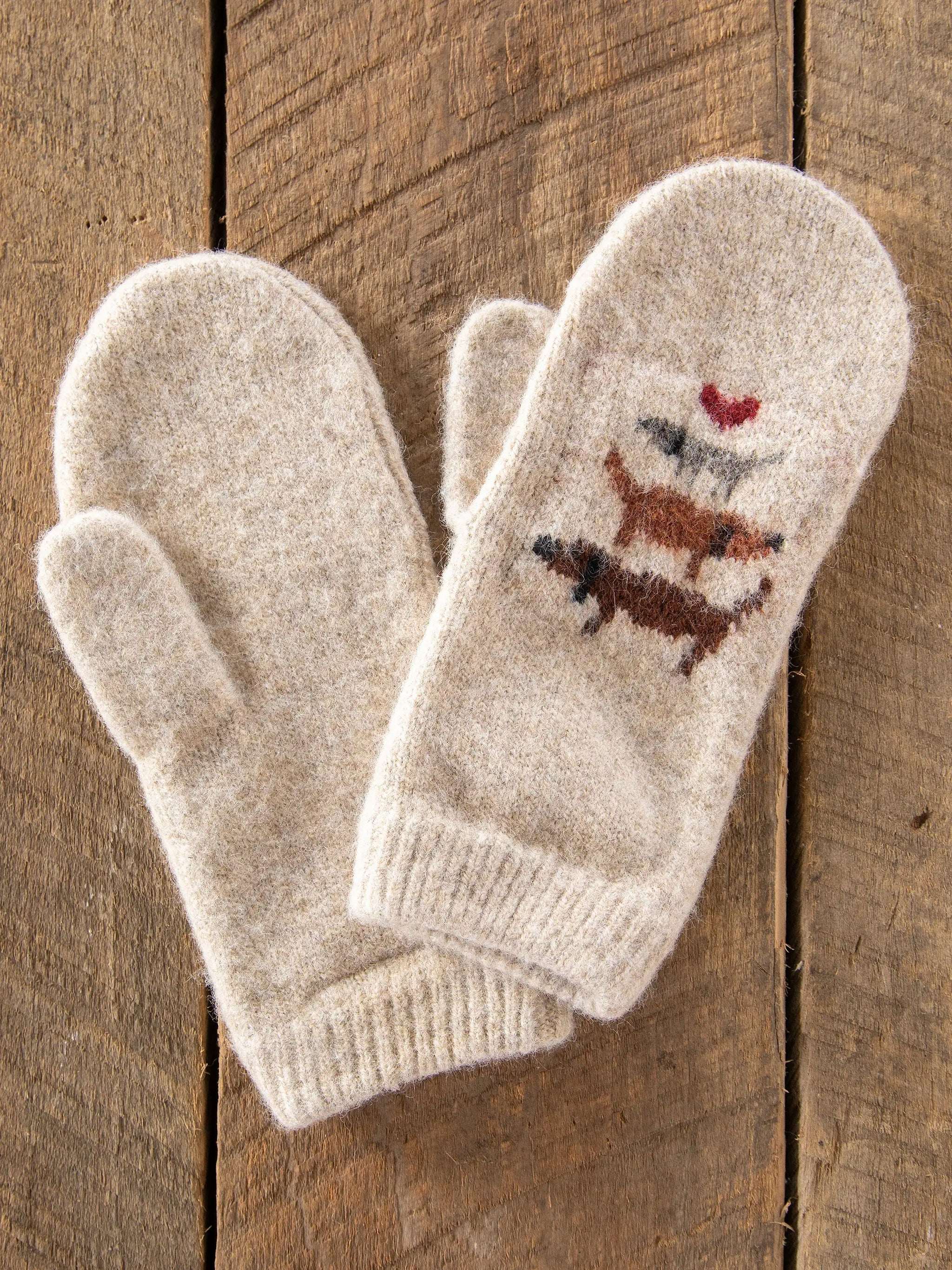 Pair of cream-colored mittens with embroidered designs on a wooden surface