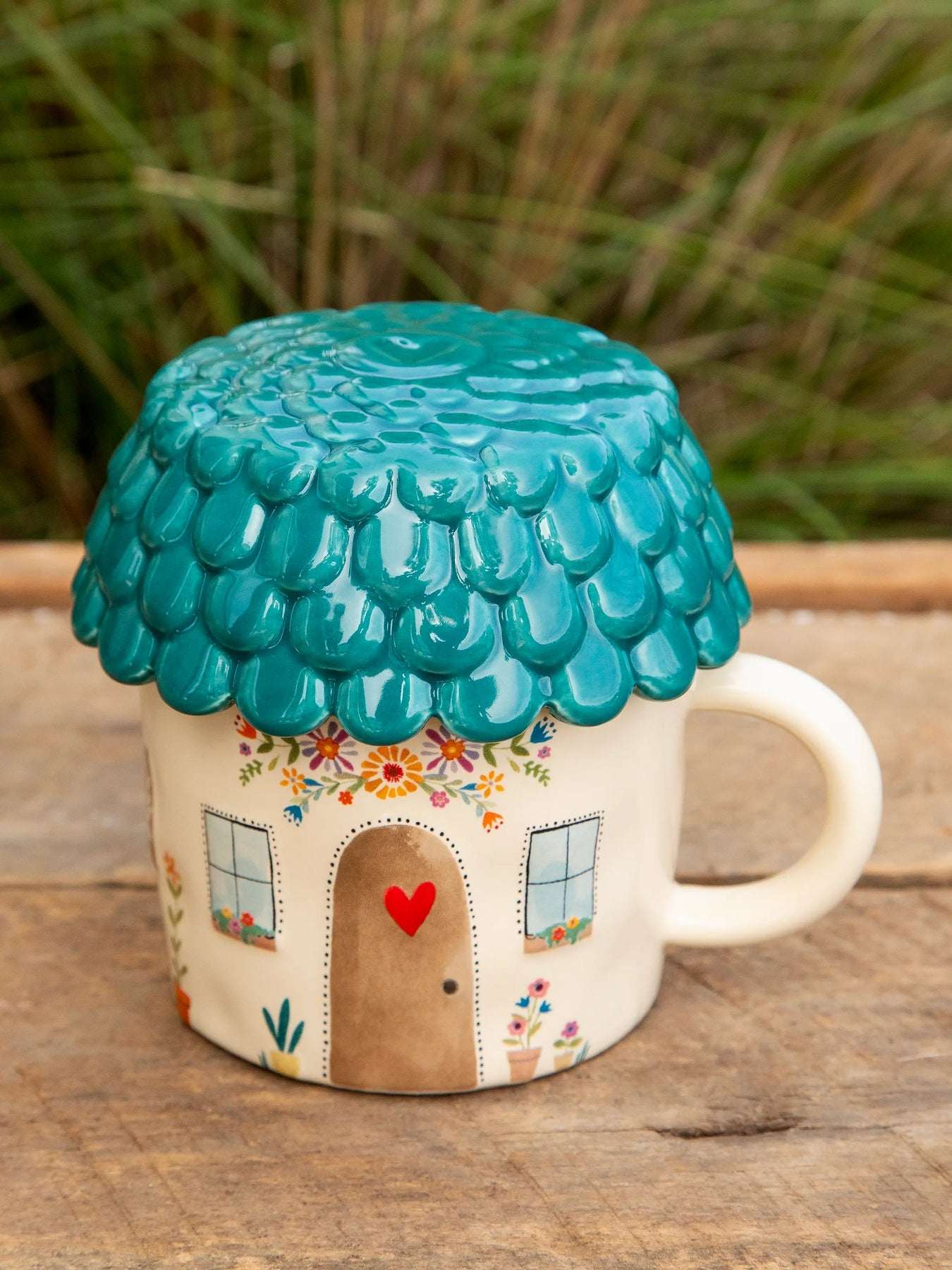 Mug shaped like a house with a teal roof on a wooden surface