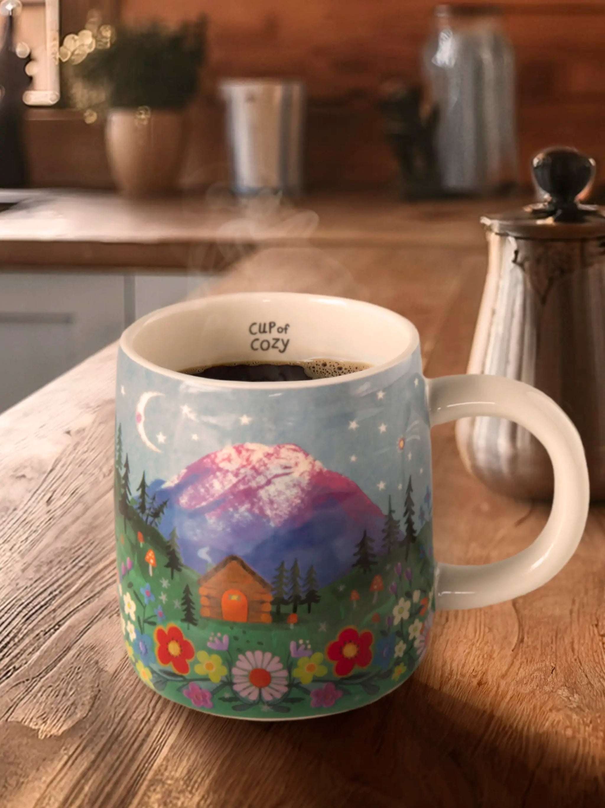 Decorative mug with a nature scene on a wooden table in a kitchen.
