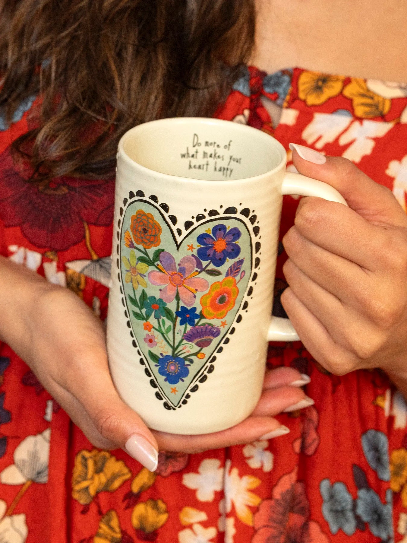 Person holding a mug with floral design and text, wearing a red floral dress.
