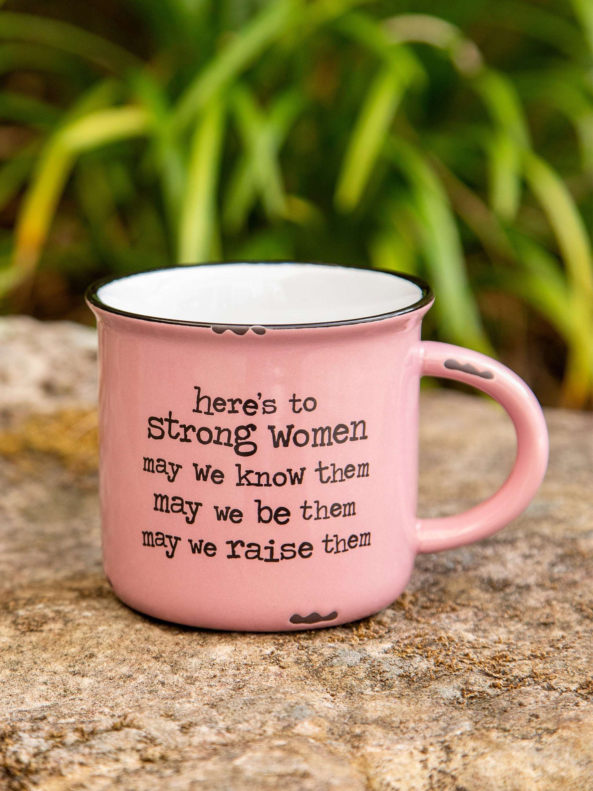 Pink mug with motivational quote on a stone surface with greenery in the background