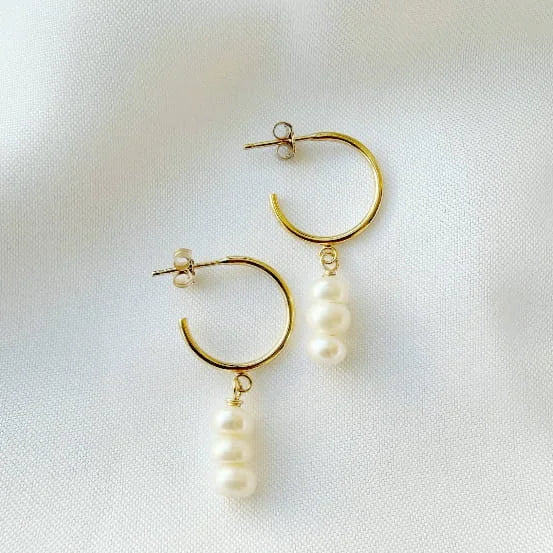 Gold hoop earrings with pearl drops on a white fabric background