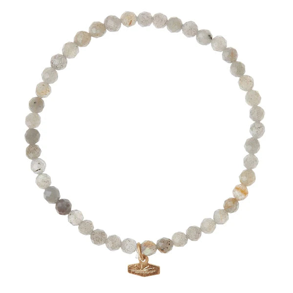 A faceted semi-precious gemstone bracelet with a brass logo charm, presented on a white background.