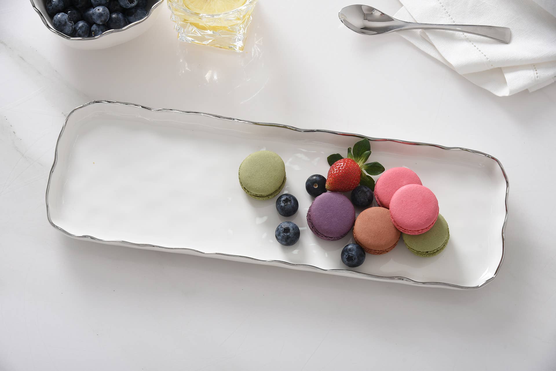 Colorful macarons on a white plate with a white napkin and silver spoon in the background.