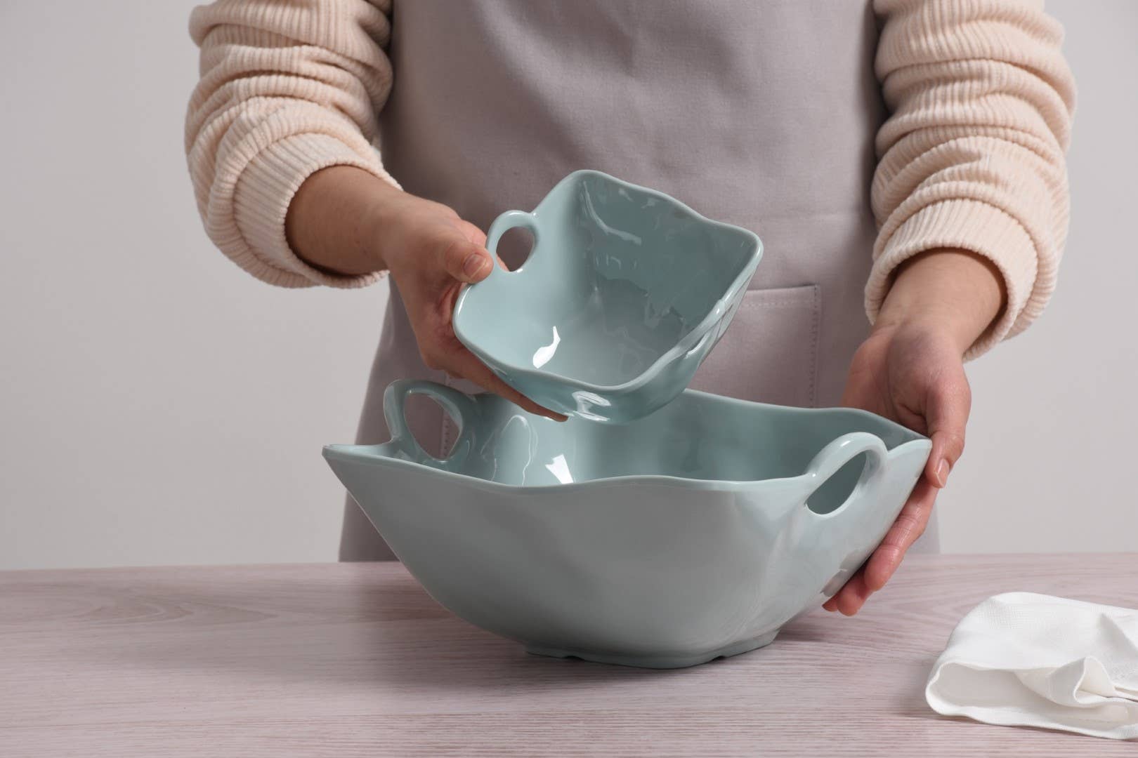 Person holding a light blue ceramic bowl with handles on a neutral background