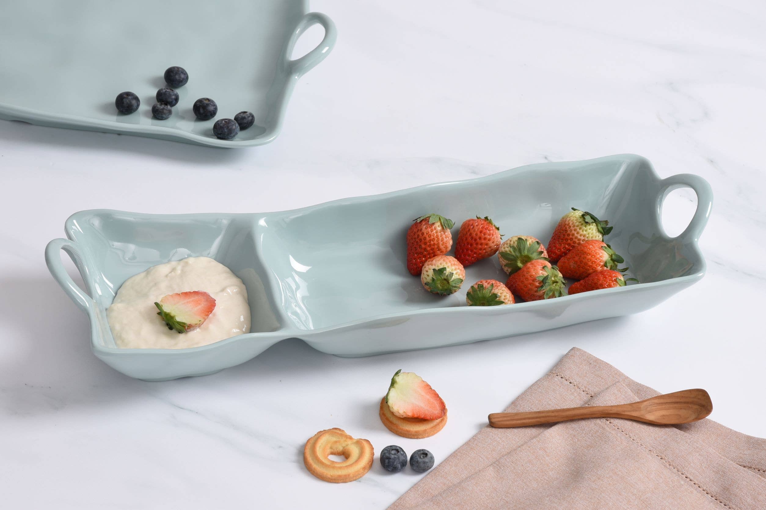 Light blue ceramic dish with compartments containing strawberries, cookies, and a napkin on a white background