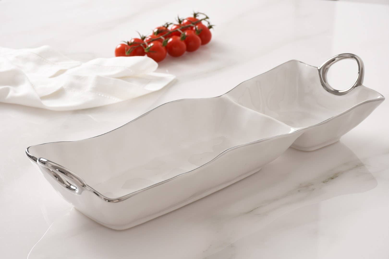 Silver serving dish with two compartments on a white surface with cherry tomatoes.