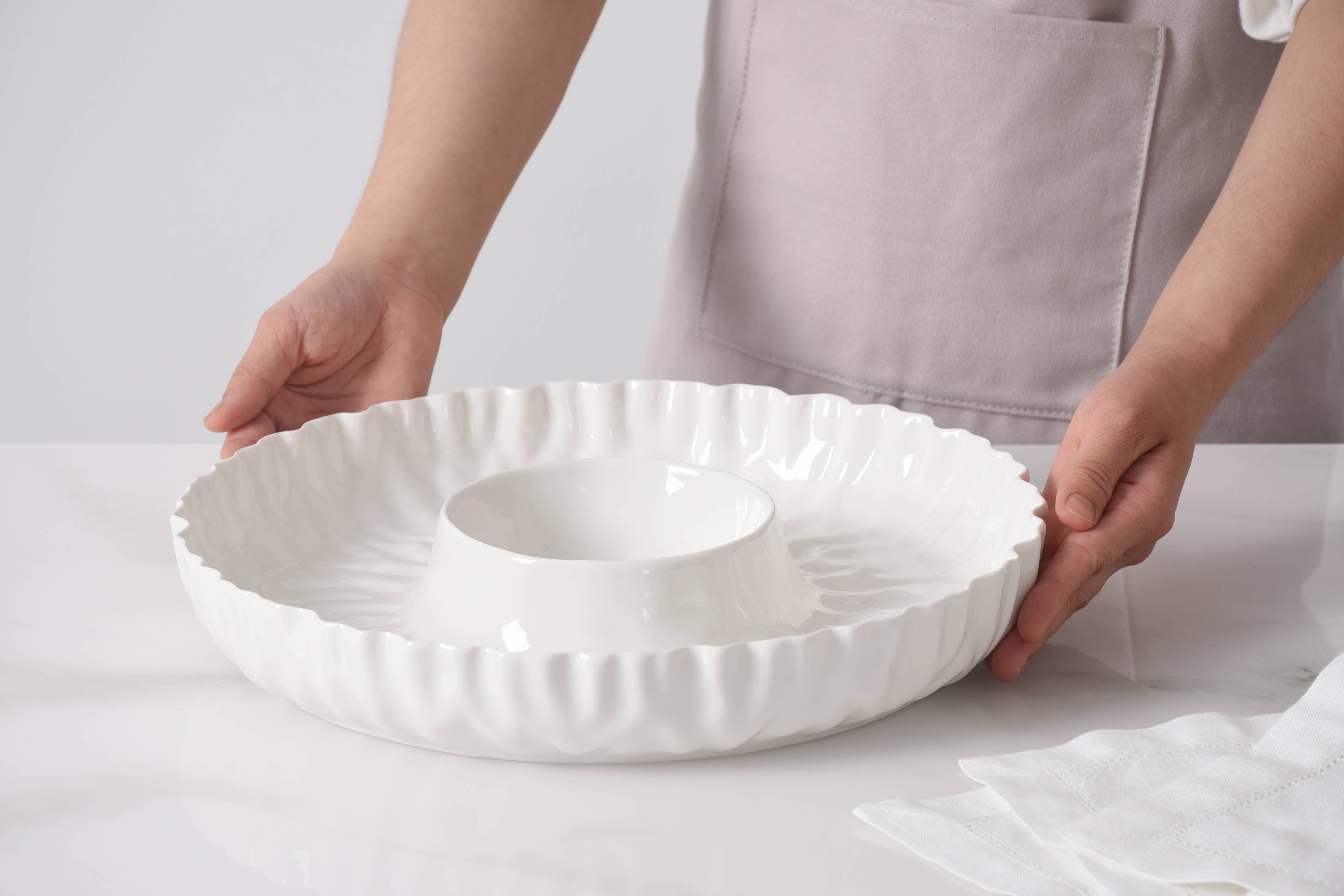 Person holding a white ceramic dish with decorative edge on a light background