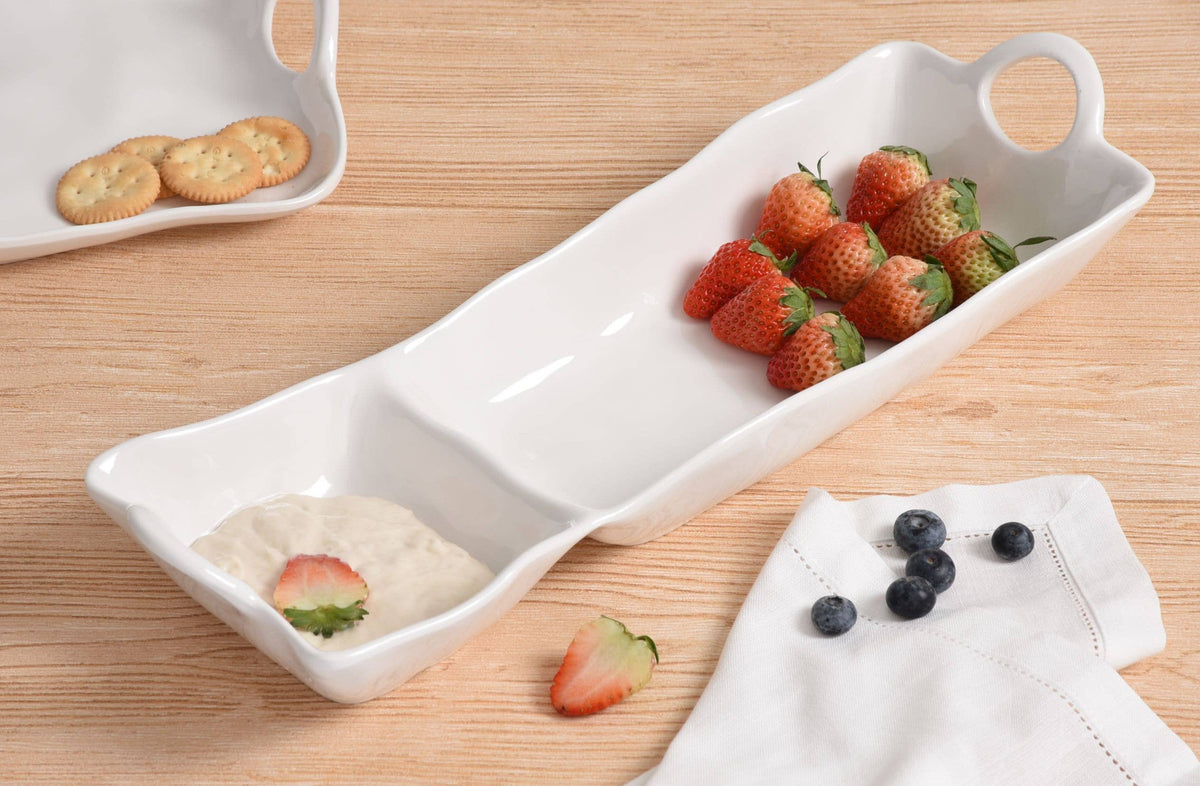 White ceramic tray with compartments holding strawberries, crackers, and a napkin on a wooden surface.