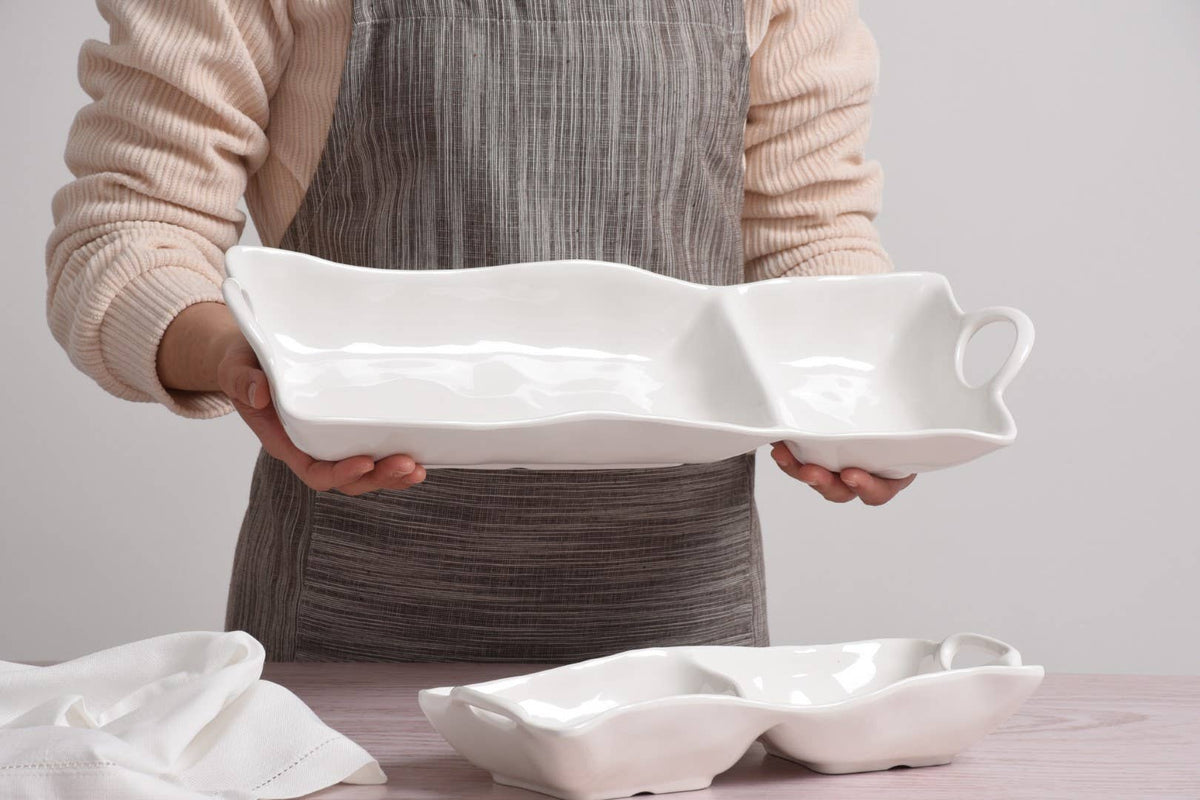 Person holding a white ceramic serving tray with handles on a neutral background