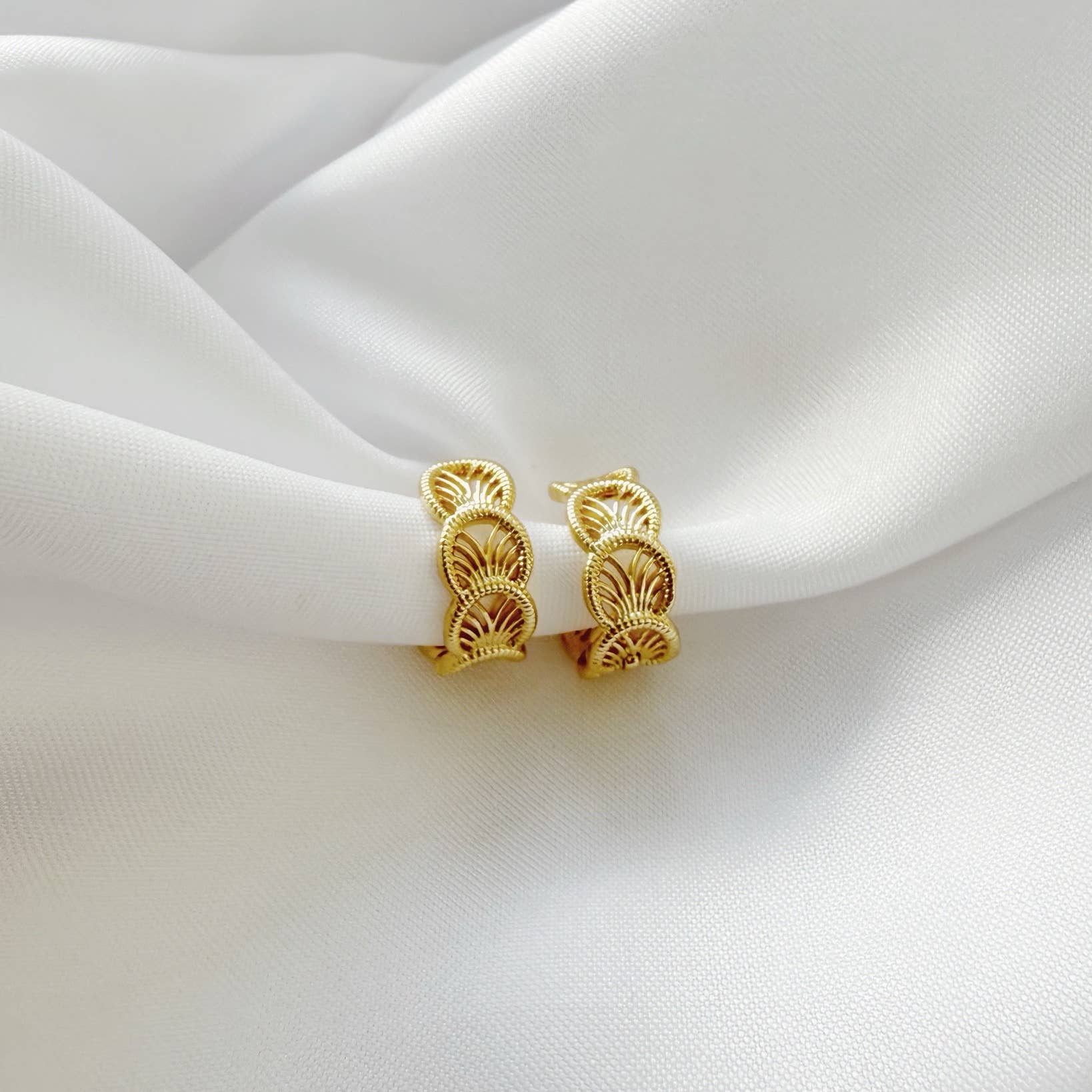 Gold hoop earrings on a white fabric background