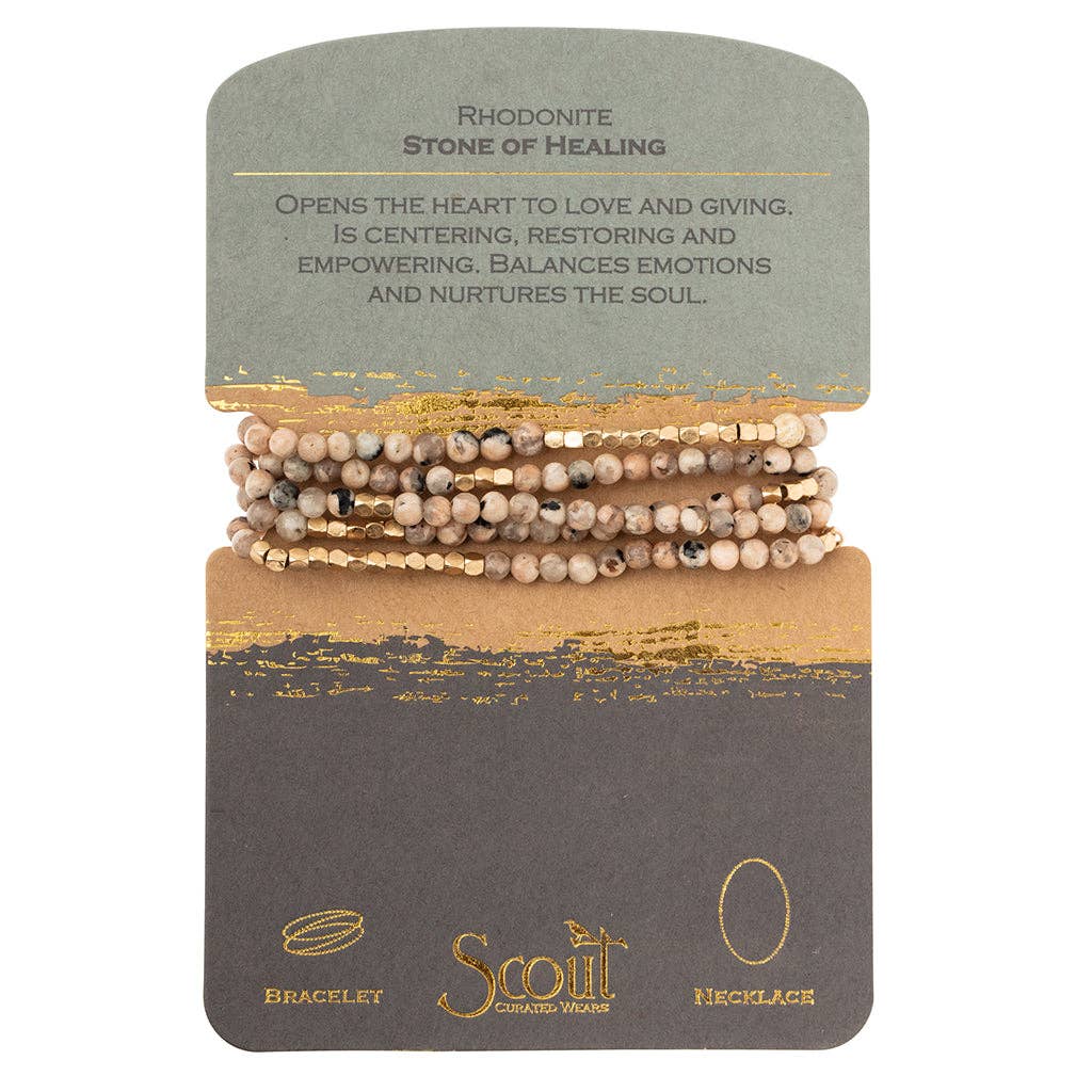 A card with a bracelet design featuring semi-precious stone beads and plated brass, wrapped in a cord. The card has text describing the rhodonite stone as 'Stone of Healing' and indicates the product is by the brand Scout.