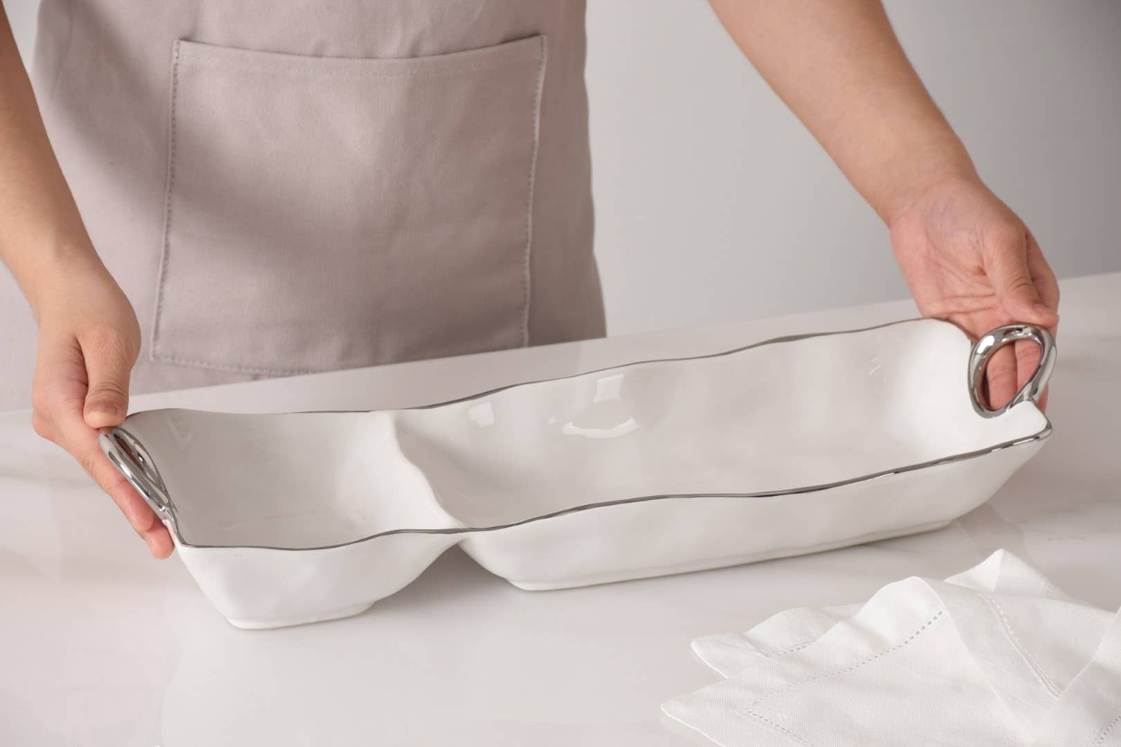 Person holding a large white baking dish with a gray interior on a light background
