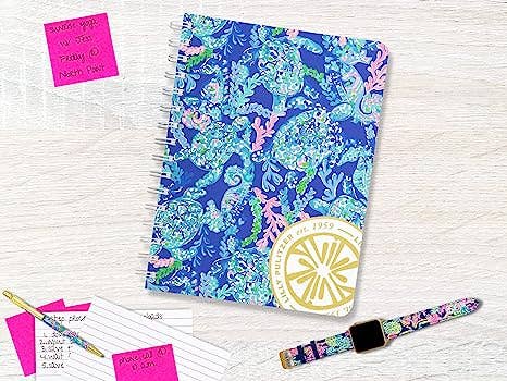 Notebook with a colorful coral pattern, pen, and watch on a light wooden surface.