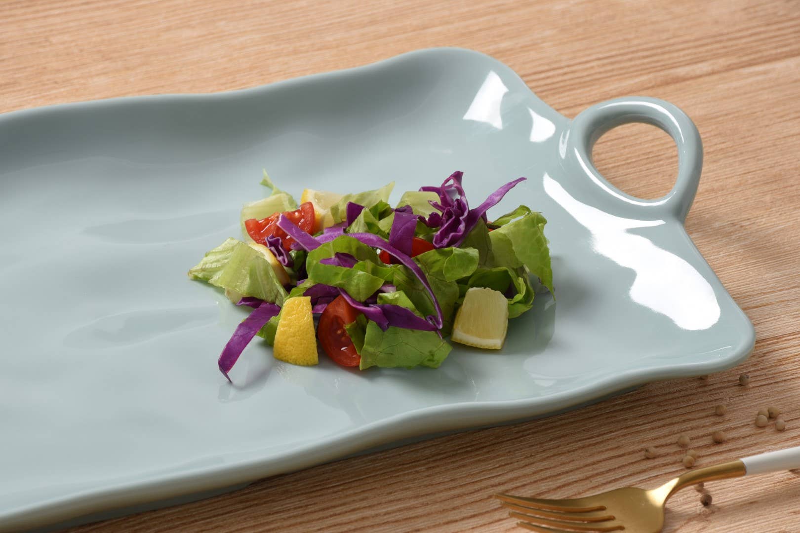 Salad on a gray ceramic platter with a handle on a wooden table.