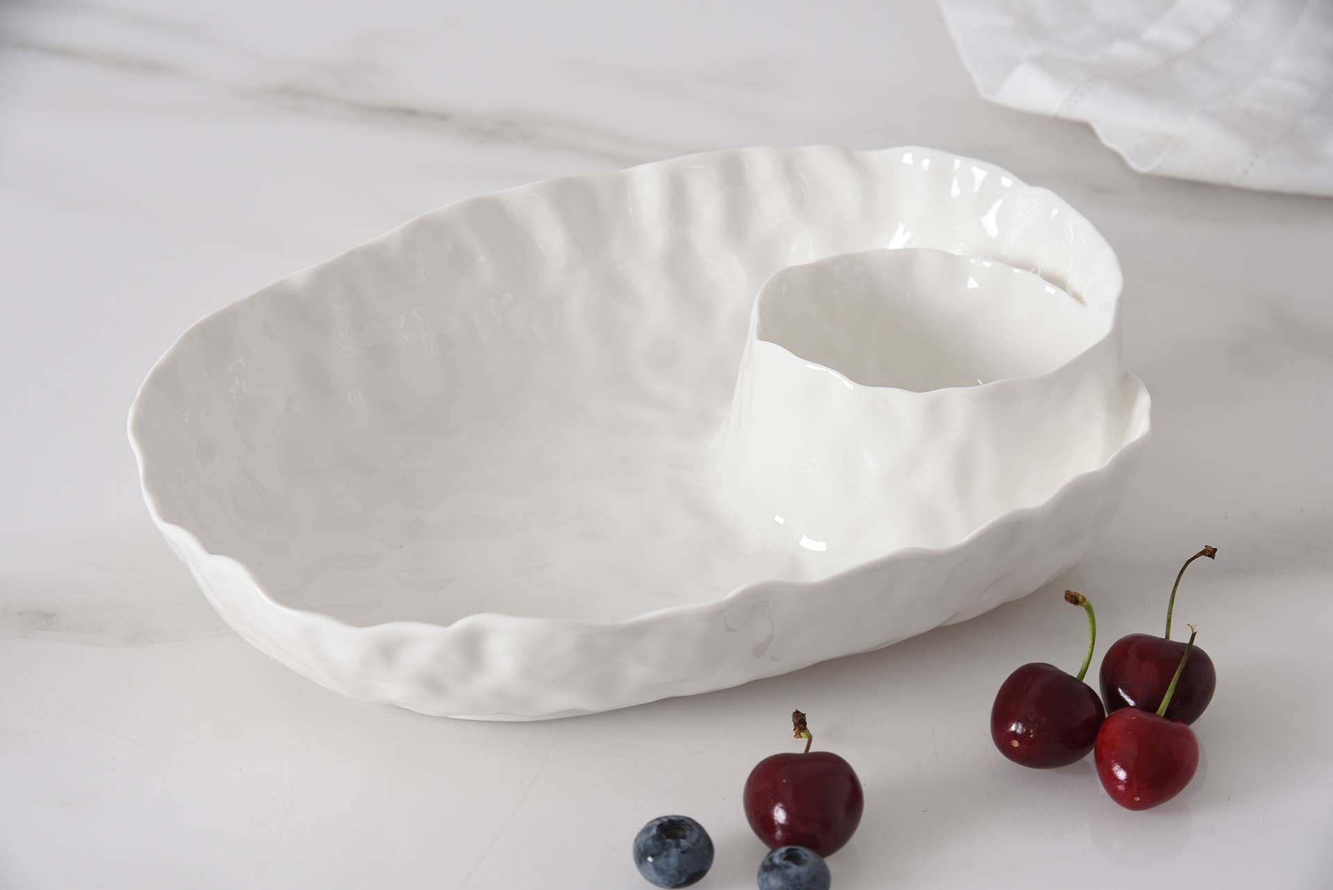 White ceramic bowl on a white surface with cherries and blueberries.